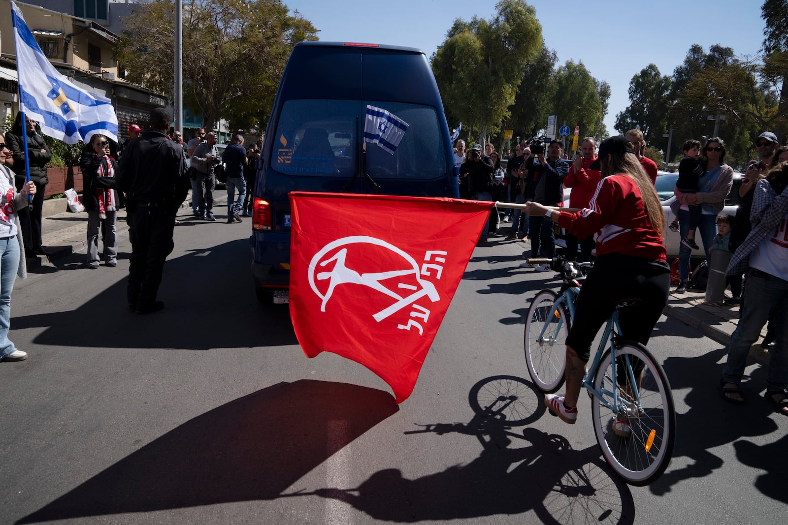 People attend a public memorial ceremony for slain hostage Tsachi Idan, a fan of Hapoel Tel Aviv F.C., who was killed in Hamas captivity in the Gaza Strip, watch a van carrying his coffin outside of Bloomfield Stadium in Tel Aviv, Israel, Friday, Feb. 28, 2025. (AP Photo/Leo Correa)