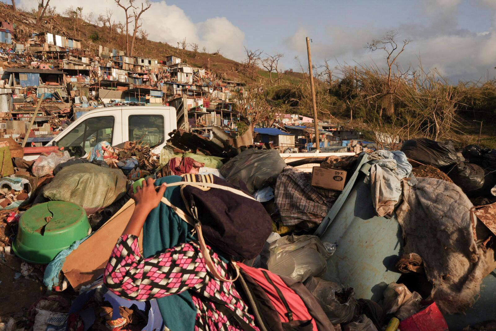 A woman carrying her belongings walks past debris after Cyclone Chido in the Kaweni slum Thursday, Dec. 19, 2024, on the outskirts of Mamoudzou, in the French Indian Ocean island of Mayotte. (AP Photo/Adrienne Surprenant)