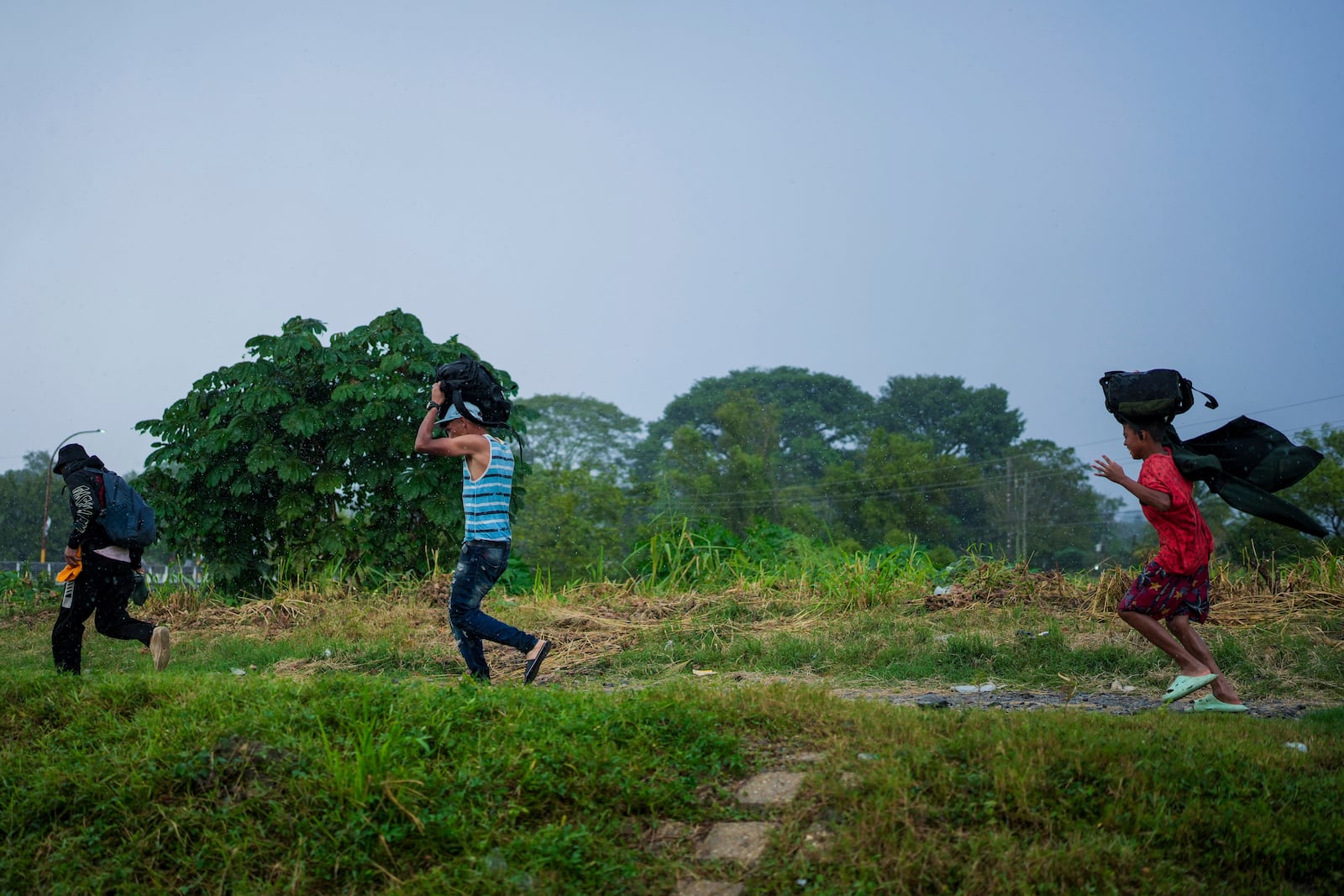 Migrants run in the rain after arriving at a makeshift shelter in Huixtla, Chiapas state, Mexico, Wednesday, Nov. 6, 2024, hoping to reach the country's northern border and ultimately the United States. (AP Photo/Moises Castillo)