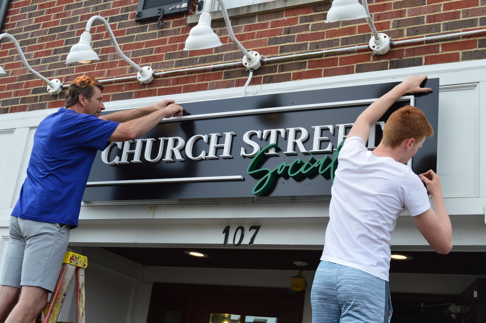 Employees from Signery2 install the new Church Street Social sign over the door for the business which has changed its name but keeps many of the fun events which made the former Books & Brews popular. A new menu by a new chef is the biggest change at the 107 E. Church St. location. CONTRIBUTED/BOB RATTERMAN