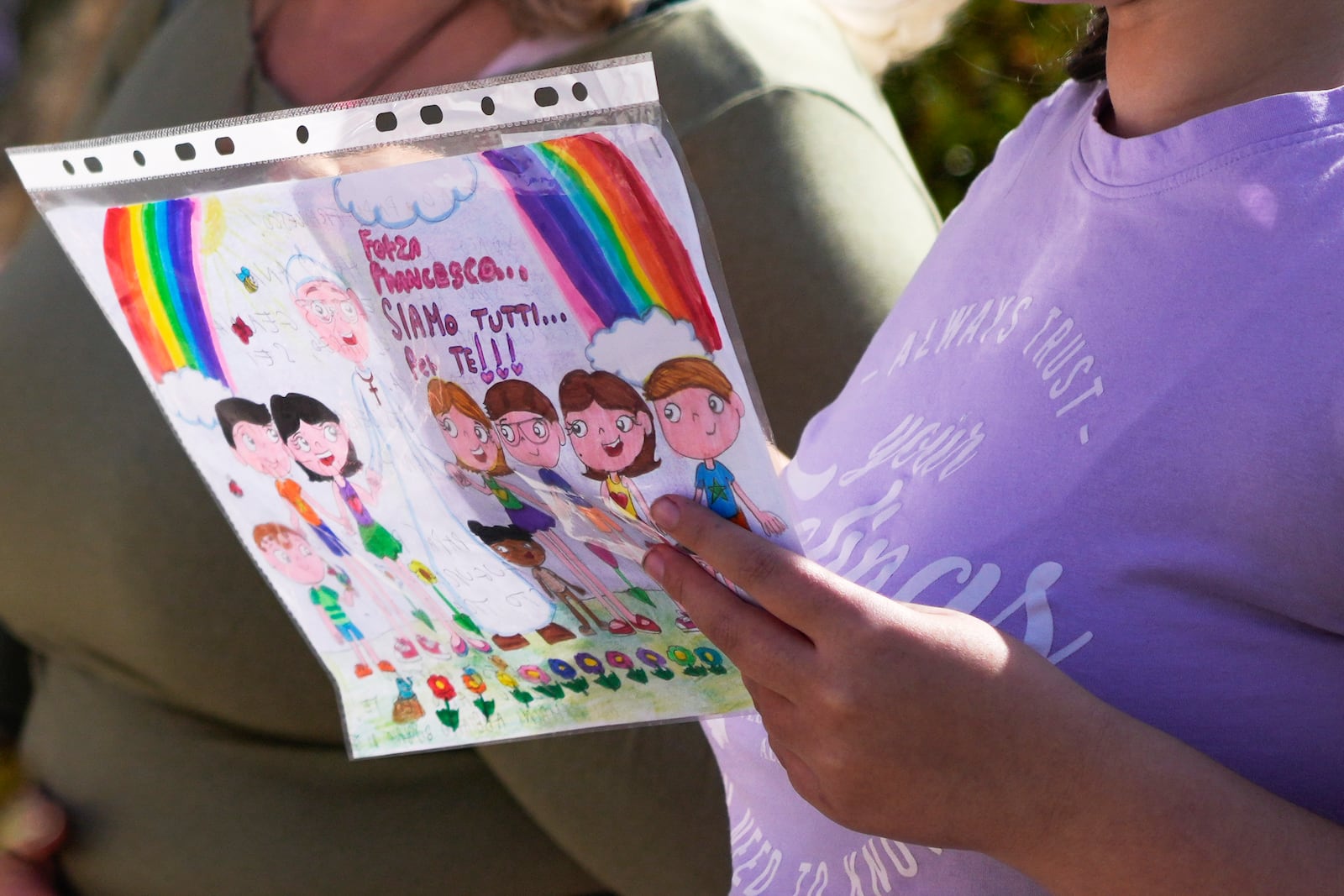 A child holds a drawing reading: "C'mon Pope Francis we are all with you" as she prays outside the Agostino Gemelli Polyclinic in Rome, Sunday, Feb. 23, 2025, where Pope Francis is hospitalized since Feb. 14. (AP Photo/Gregorio Borgia)