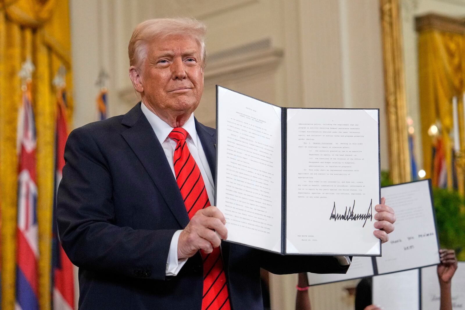 President Donald Trump holds up a signed executive order at an education event in the East Room of the White House in Washington, Thursday, March 20, 2025. (AP Photo/Ben Curtis)