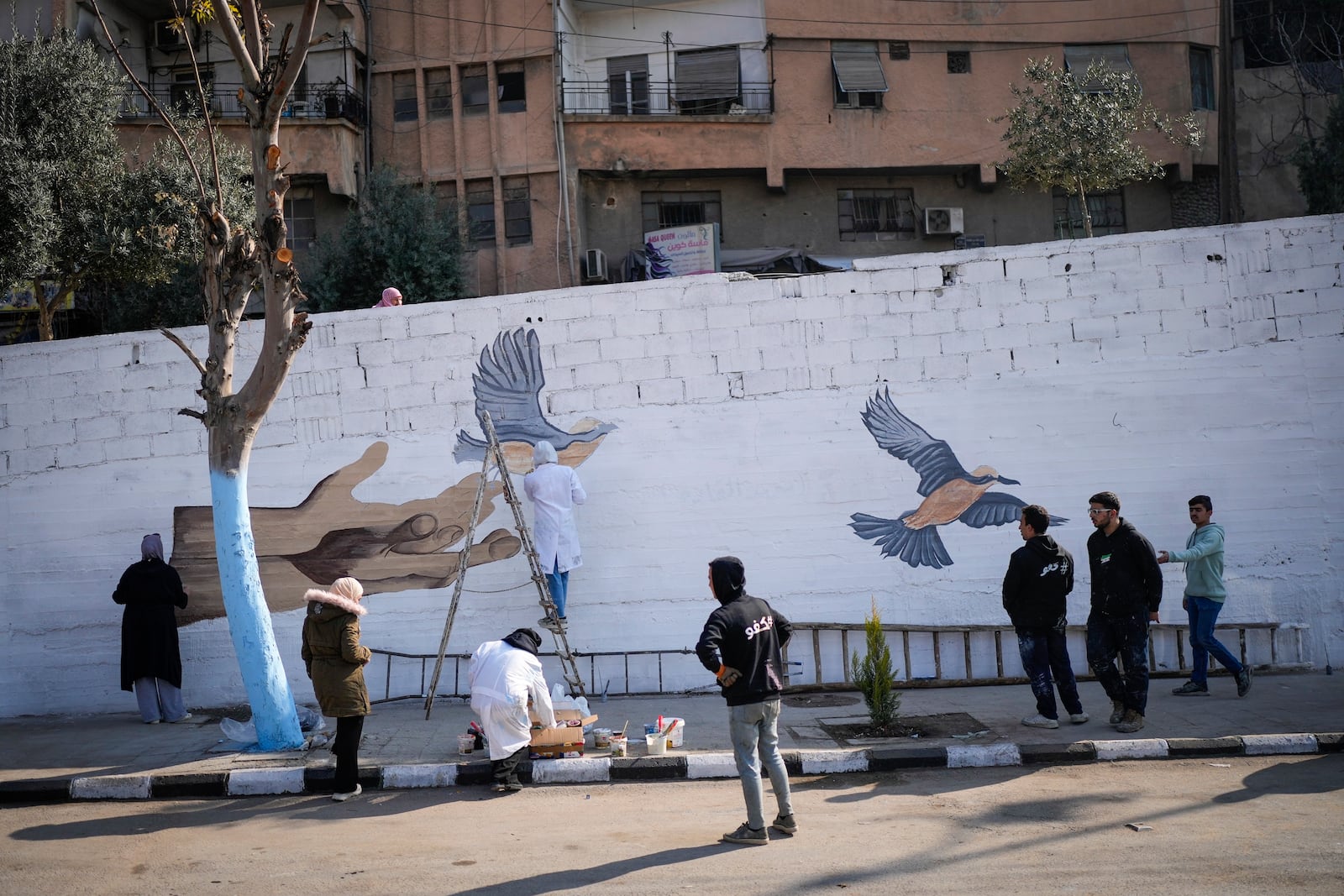 A group of young volunteers paints a mural symbolizing peace on a wall on the outskirts of Damascus, Syria, Sunday, Jan. 12, 2025. (AP Photo/Mosa'ab Elshamy)