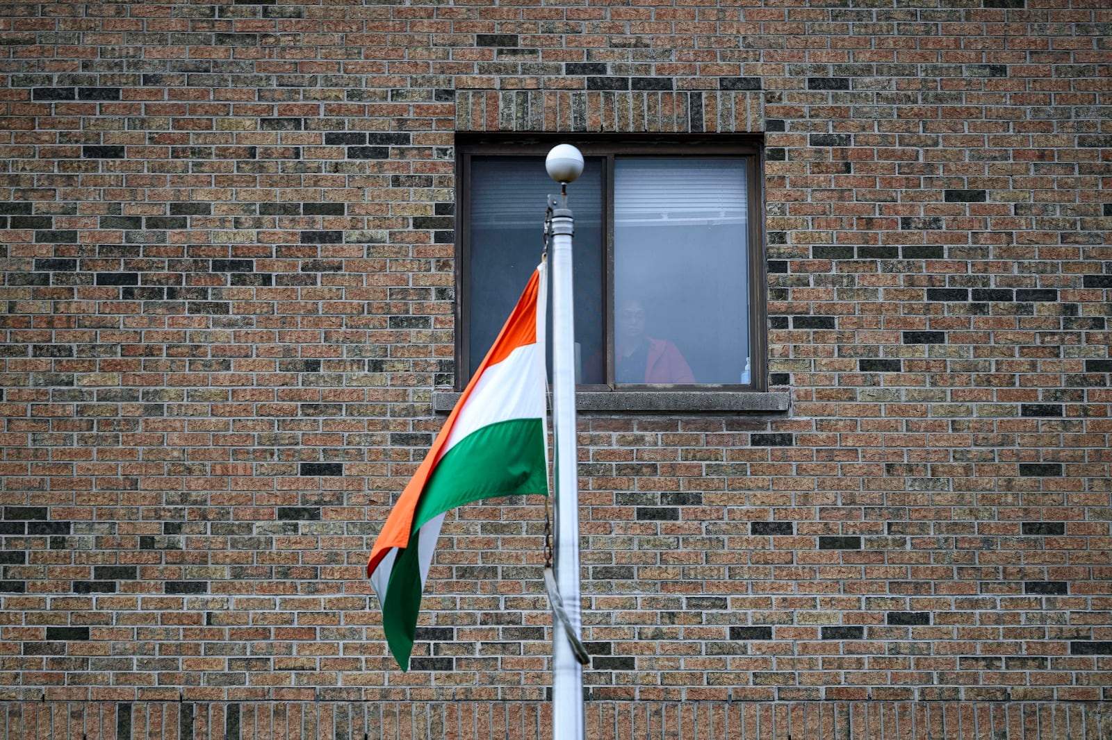 The flag of India flies in front of a person standing at a window, at The High Commission of India in Canada, in Ottawa, Ontario, on Monday, Oct. 14, 2024. (Justin Tang/The Canadian Press via AP)