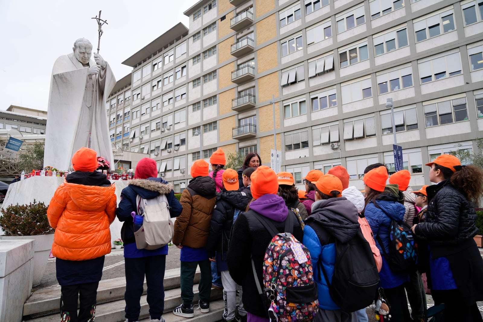 A group of children from a primary school pray for Pope Francis in front of the statue Pope John Paul II outside Agostino Gemelli Polyclinic in Rome, Wednesday, Feb. 19, 2025, where the Pontiff is hospitalized since Friday, Feb. 14. (AP Photo/Gregorio Borgia)