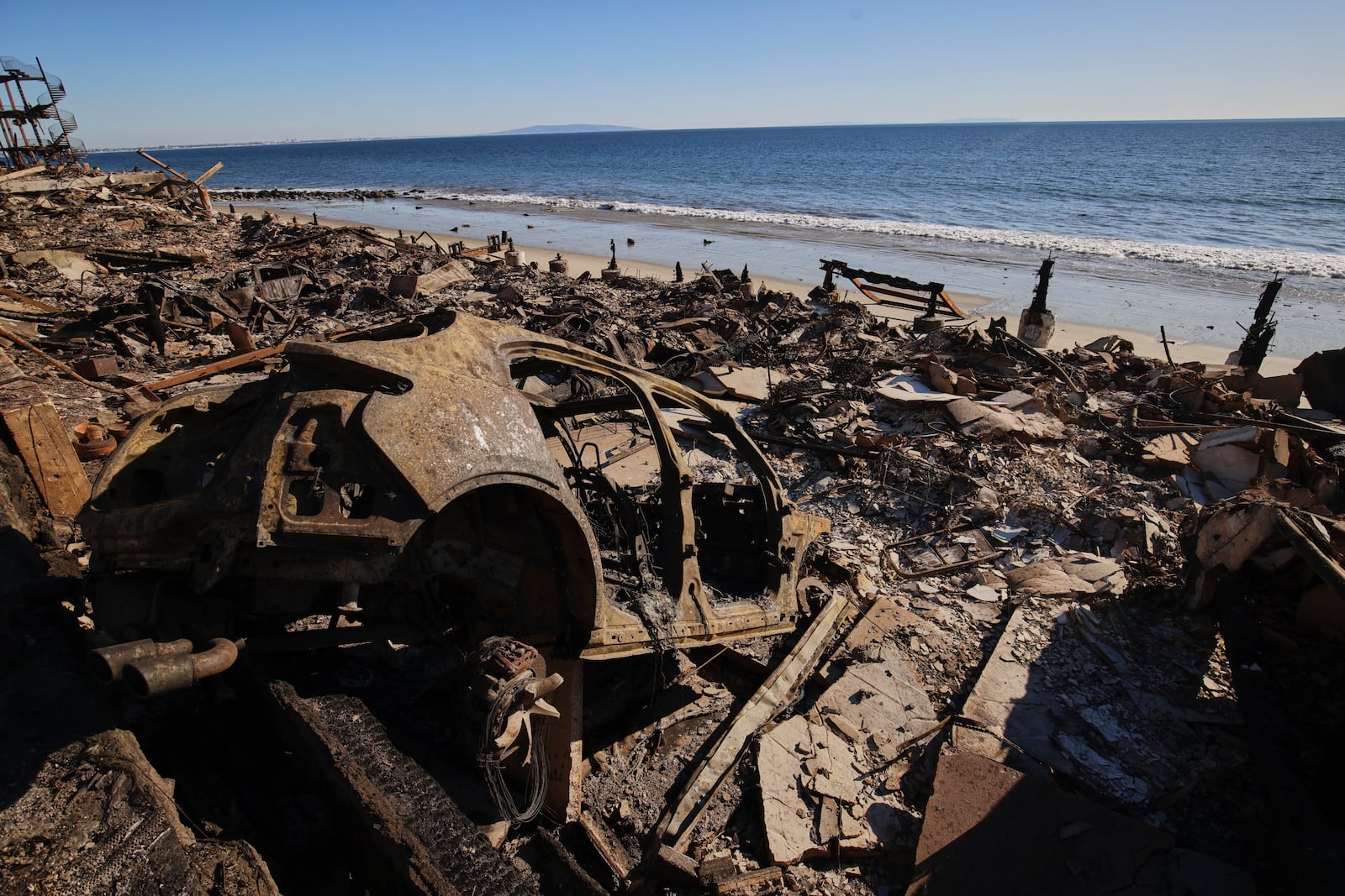 A burned car is seen among debris in the wreckage of a home destroyed by the Palisades Fire, Tuesday, Jan. 14, 2025, in Malibu, Calif. (AP Photo/Ethan Swope)