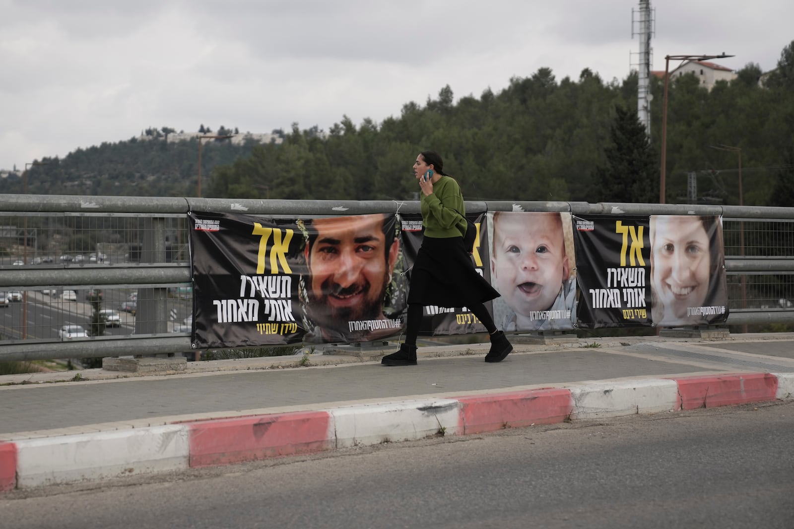 A woman walks past photos of hostages held by Hamas in the Gaza Strip, in Jerusalem, Friday, Jan. 17, 2025. (AP Photo/Mahmoud Illean)