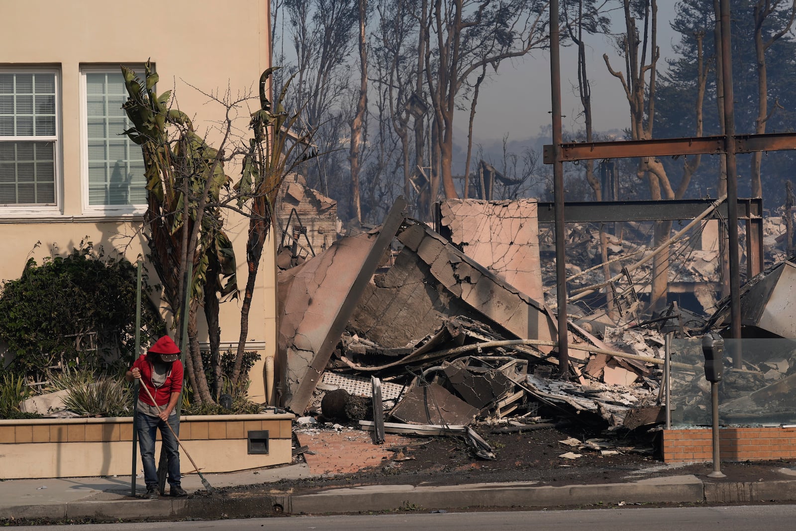 A person begins cleaning up after the Palisades Fire ravaged a neighborhood amid high winds in the Pacific Palisades neighborhood of Los Angeles, Wednesday, Jan. 8, 2025. (AP Photo/Damian Dovarganes)