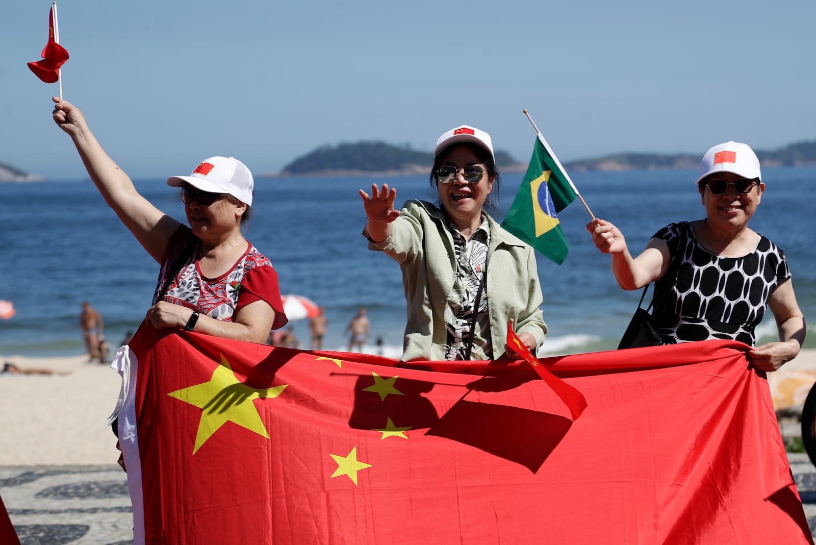 People wave Chinese and Brazilian flags as they wait for China's President Xi Jinping for him to drive past Leblon beach to his hotel during the G20 summit in Rio de Janeiro, Monday, Nov. 18, 2024. (AP Photo/Bruna Prado)