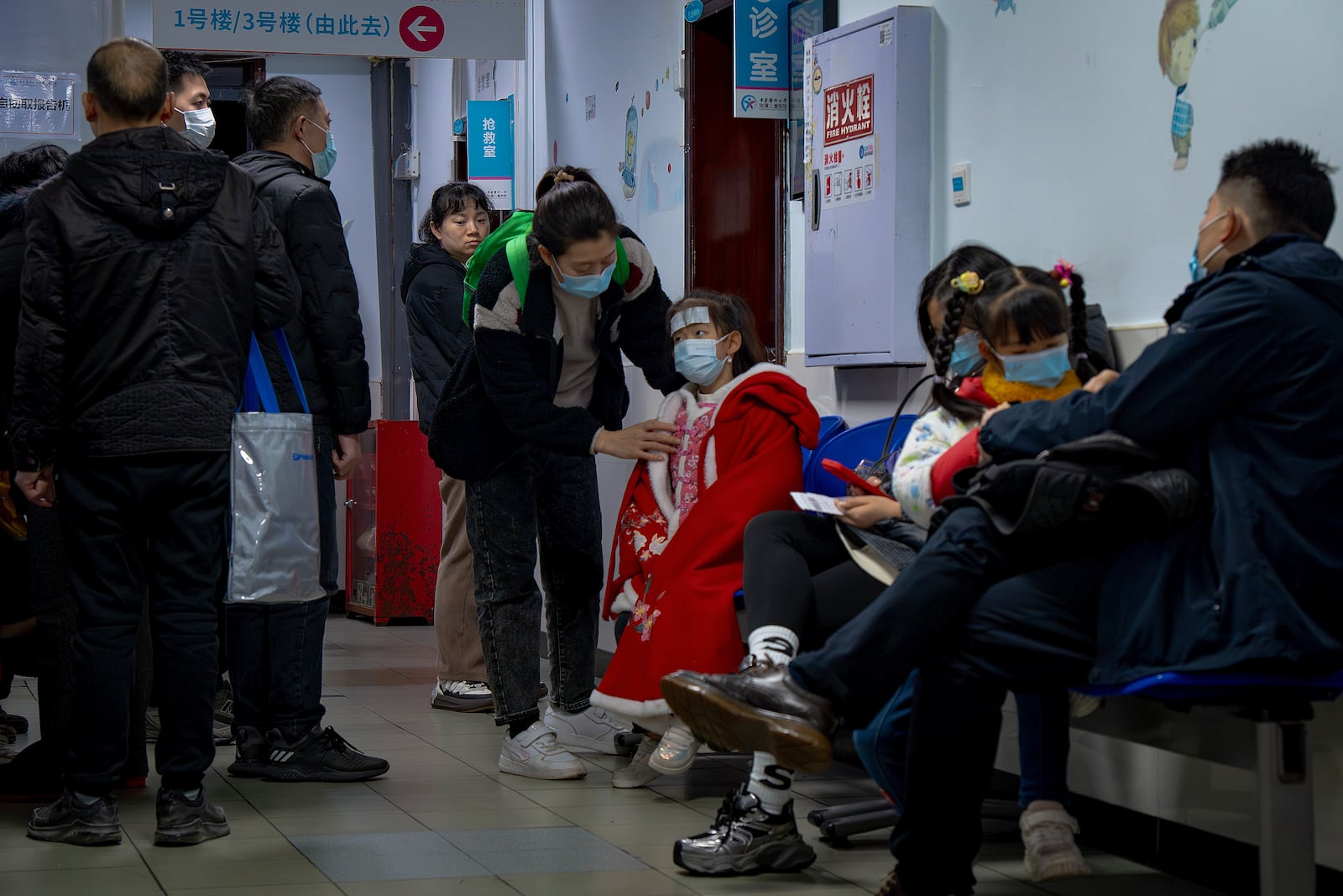 A woman wearing a face mask tends to a child at a corridor crowded with parents at a pediatric hospital in southwest China's Chongqing Municipality on Jan. 7, 2025. (Chinatopix via AP)