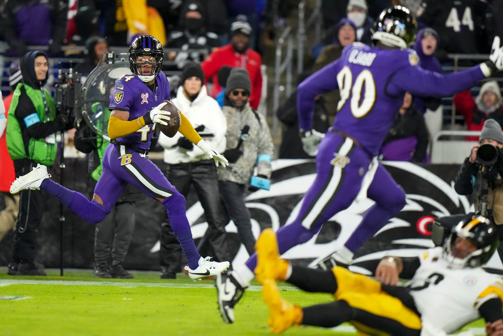 Pittsburgh Steelers quarterback Russell Wilson, bottom right, hits the turf as Baltimore Ravens cornerback Marlon Humphrey, left, returns an interception for a touchdown during the second half of an NFL football game, Saturday, Dec. 21, 2024, in Baltimore. (AP Photo/Stephanie Scarbrough)