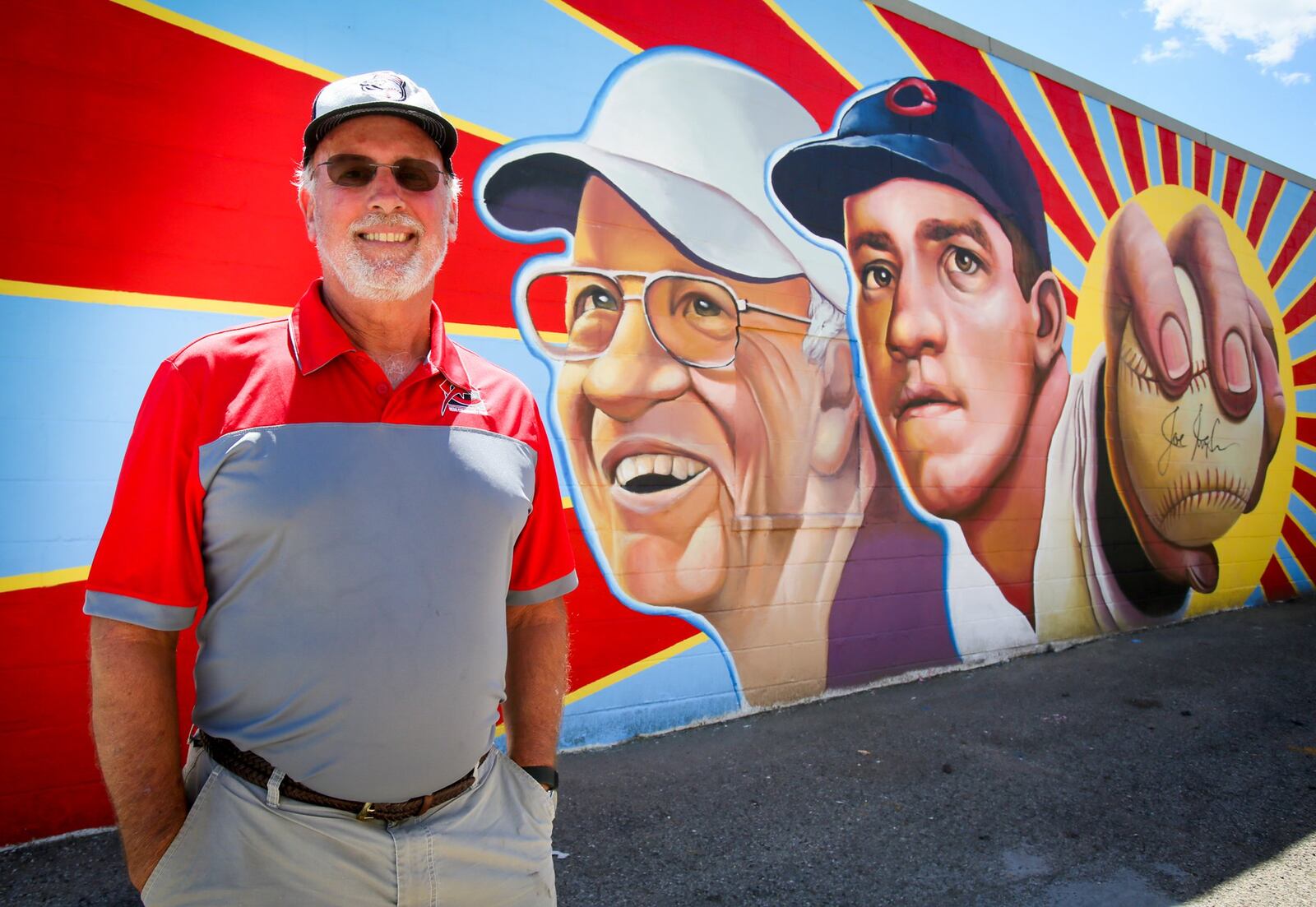 Kim Nuxhall stands with a the new Hamilton mural featuring his father, Cincinnati Reds legend, Joe Nuxhall, painted on the side of Clark’s Sporting Goods on Hamilton’s west side. GREG LYNCH / STAFF