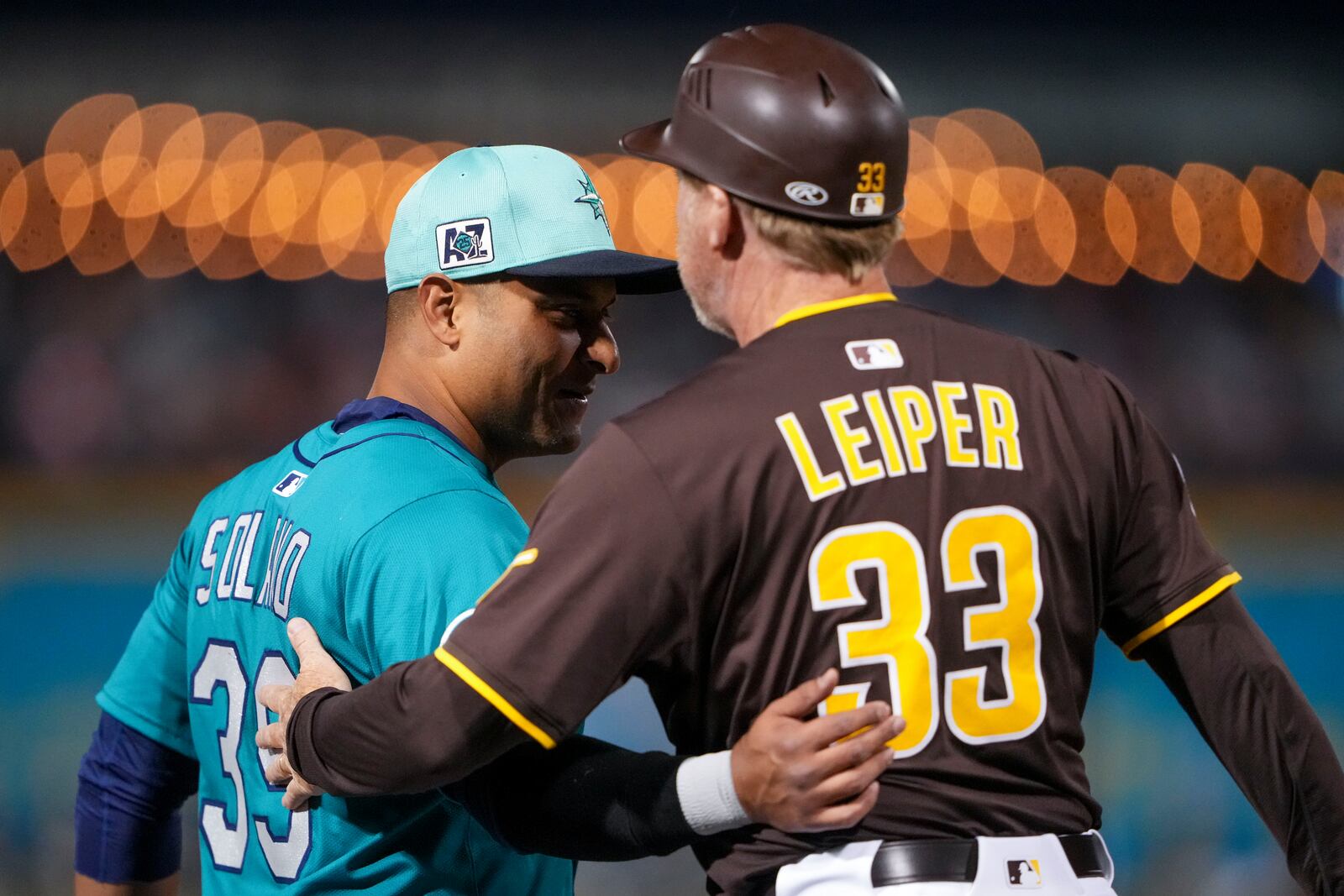 Seattle Mariners third baseman Donovan Solano, left, greets San Diego Padres third base coach, infield & base running instructor Tim Leiper, right, during a spring training baseball game Friday, Feb. 28, 2025, in Peoria, Ariz. (AP Photo/Lindsey Wasson)