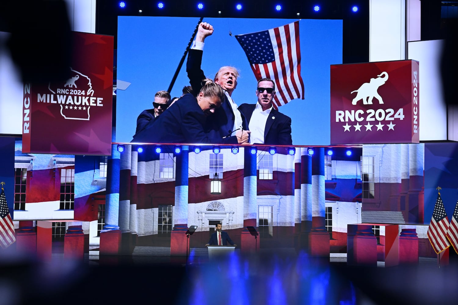 
                        An image of former President Donald after Saturday’s shooting is displayed as Donald Trump Jr. speaks on the third night of the Republican National Convention at the Fiserv Forum in Milwaukee, on Wednesday, July 17, 2024. (Kenny Holston/The New York Times)
                      