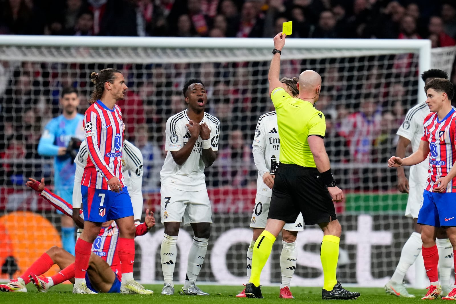 Referee Szymon Marciniak shows a yellow card to Real Madrid's Vinicius Junior during the Champions League round of 16, second leg, soccer match between Atletico Madrid and Real Madrid at the Metropolitano stadium in Madrid, Spain, Wednesday, March 12, 2025. (AP Photo/Manu Fernandez)