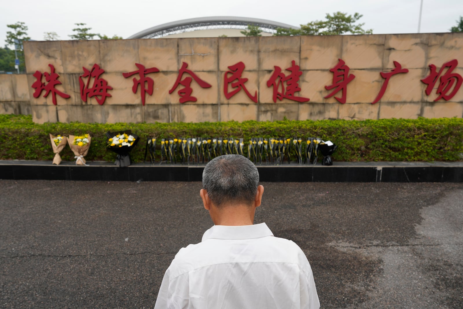 A man stands near flowers laid outside the "Zhuhai People's Fitness Plaza" where a man rammed his car into people exercising at the sports center, in Zhuhai in southern China's Guangdong province on Wednesday, Nov. 13, 2024. (AP Photo/Ng Han Guan)