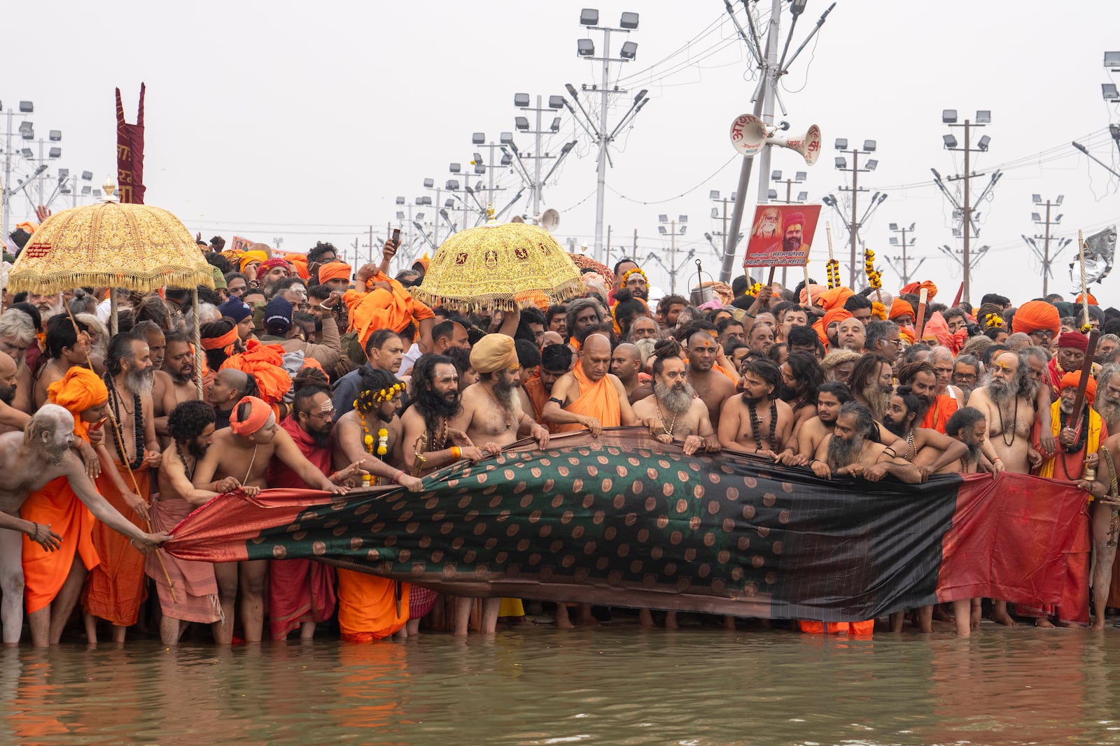 Hindu ascetics and holy men and their guru offer a cloth to the water as the prepare to bathe at the confluence of the Ganges, the Yamuna and the mythical Saraswati rivers on the second day of the 45-day-long Maha Kumbh festival in Prayagraj, India, Tuesday, Jan. 14, 2025. (AP Photo/Ashwini Bhatia)