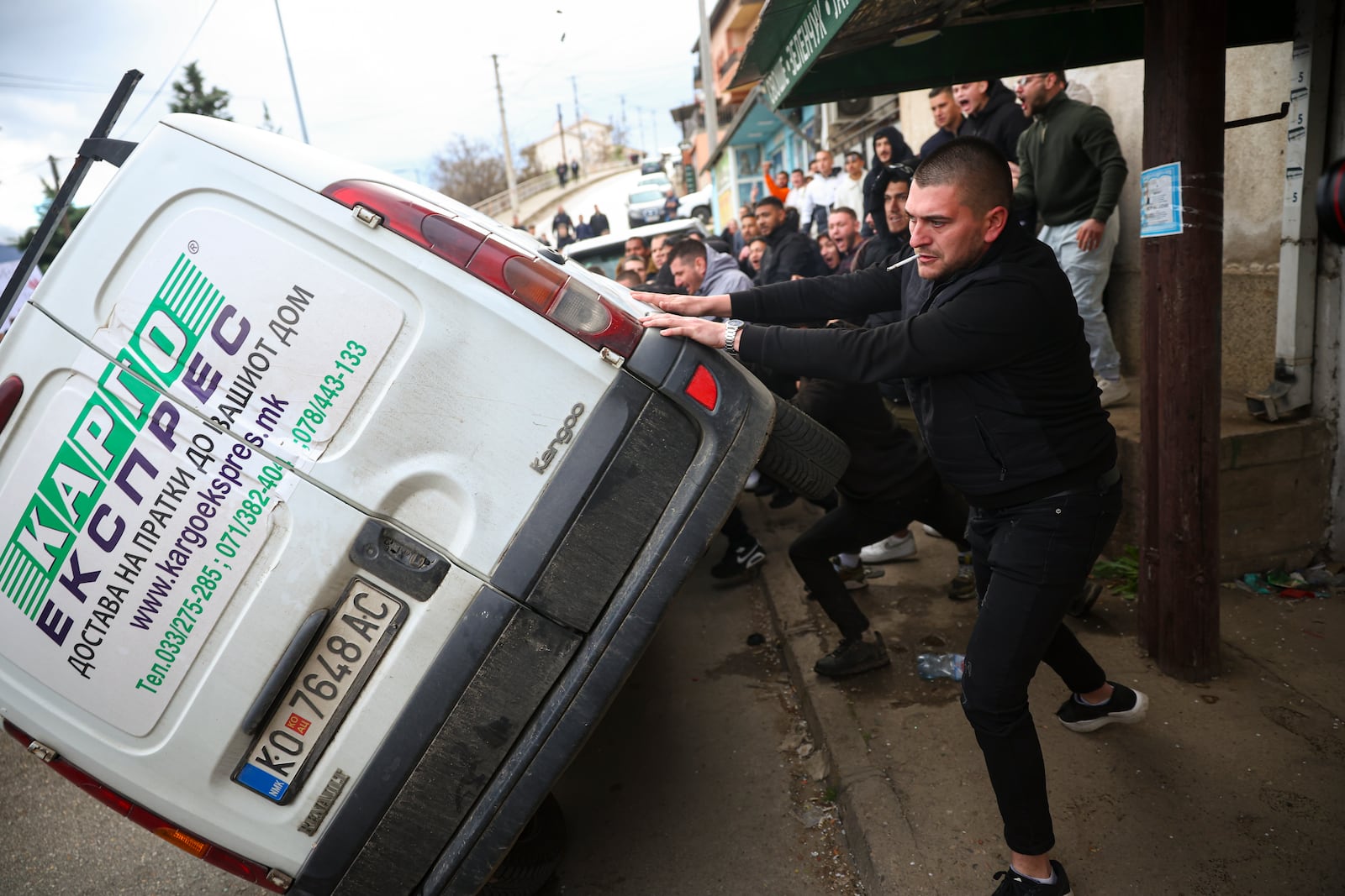 People push a car on its side while protesting near the home of the owner of a nightclub that was the scene of a massive fire, after a vigil for the victims in the town of Kocani, North Macedonia, Monday, March 17, 2025. (AP Photo/Armin Durgut)