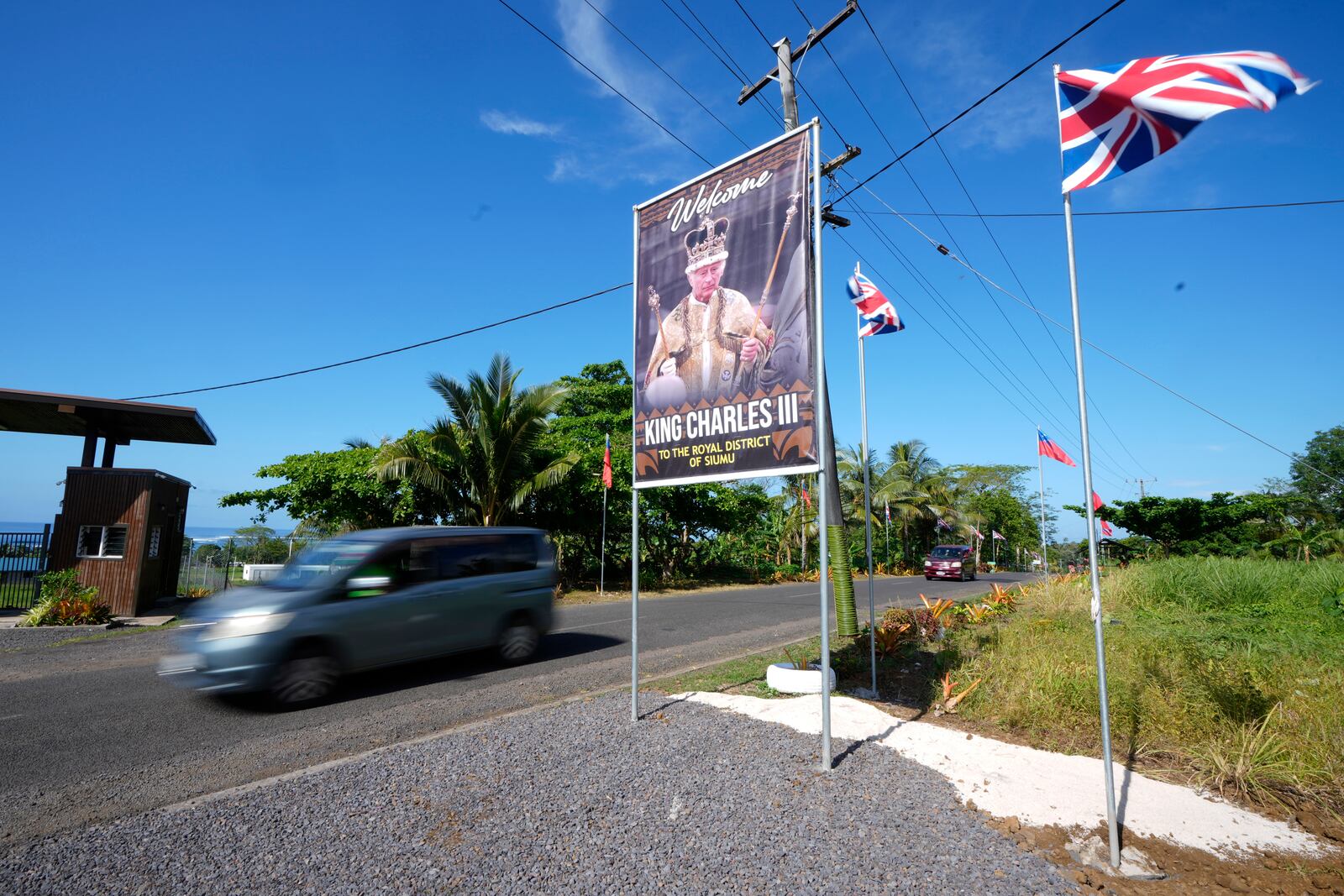 A car drives on a road decorated with flags and a portrait in the village of Siumu, Samoa, on Monday, Oct. 21, 2024, as the village prepares for the arrival of King Charles III. (AP Photo/Rick Rycroft)