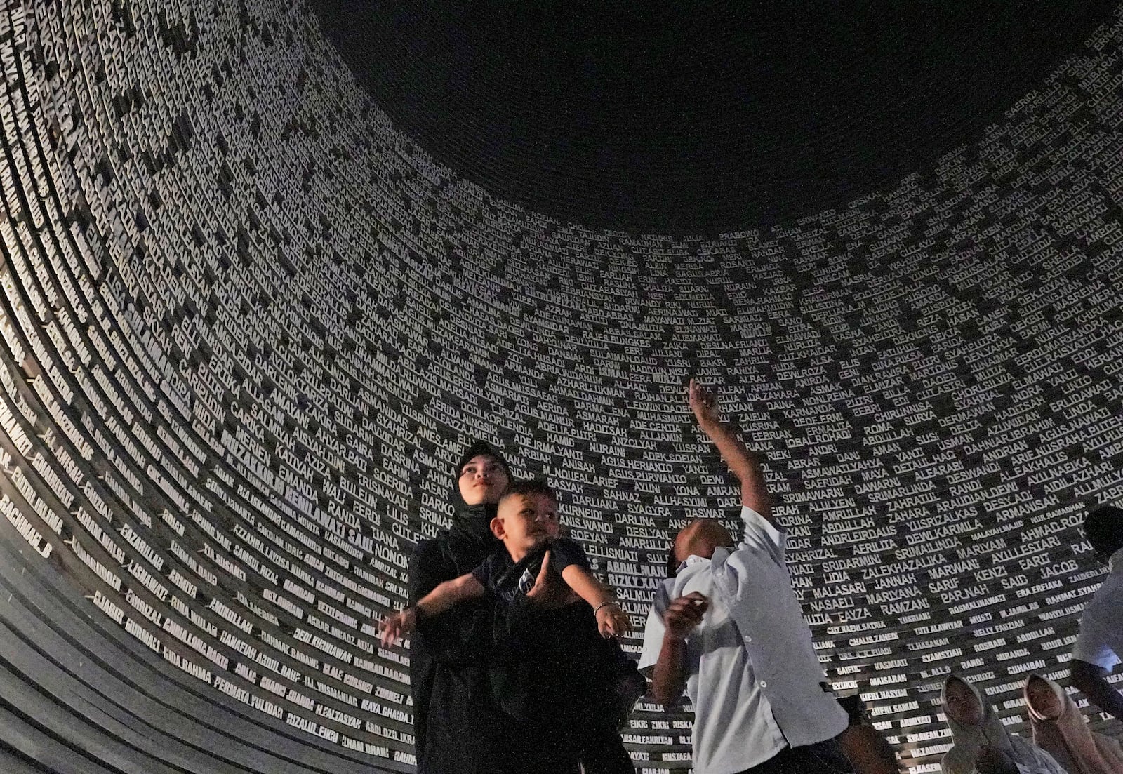 Visitors looks at a wall displaying the names of the victims of 2004 Indian Ocean tsunami, at the Tsunami Museum in Banda Aceh, Aceh province, Indonesia, Saturday, Dec 14, 2024. (AP Photo/Achmad Ibrahim)