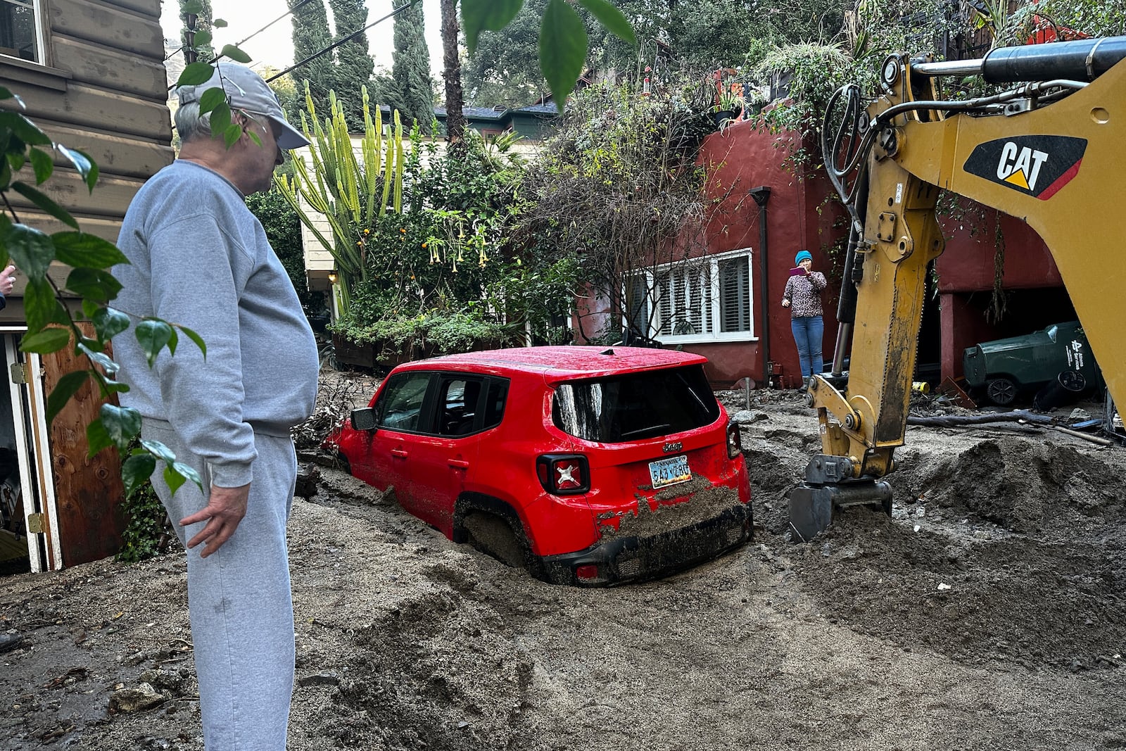 Residents watch as a vehicle is dug out of the mud after a storm Friday, Feb. 14, 2025, in Sierra Madre, Calif. (AP Photo/Eugene Garcia)