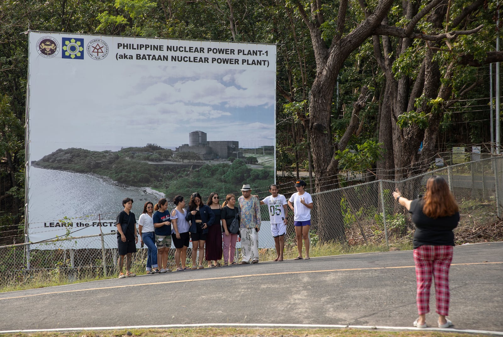 Filipino tourists pose for a photo in front of the billboard advertising the Bataan Nuclear Power Plant in the Philippines on Sunday, Jan. 19, 2025. (AP Photo/Anton L. Delgado)