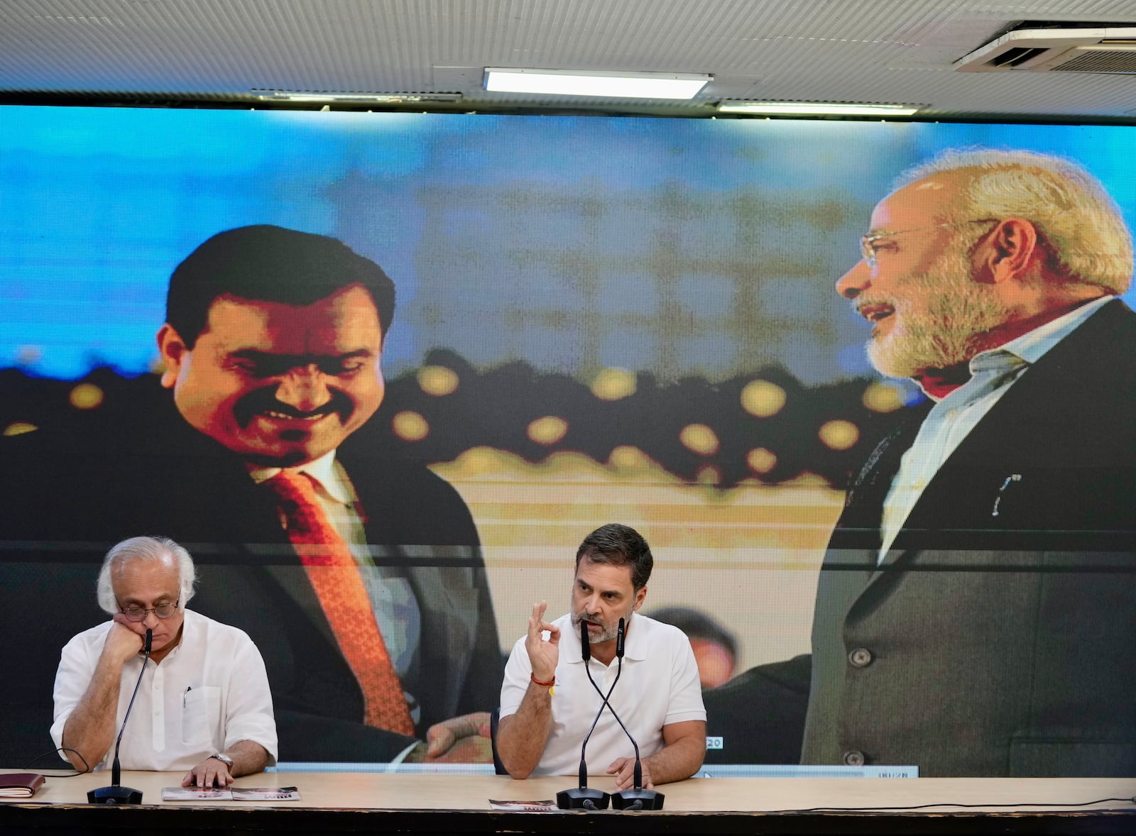 India's opposition Congress party leader Rahul Gandhi, center, addresses the media on Indian businessman Gautam Adani, after Adani was indicted by U.S. prosecutors on charges he duped investors in a massive solar energy project in India, in New Delhi, India, Thursday, Nov. 21, 2024. Image behind shows Adani, on left with Indian Prime Minister Narendra Modi, on right. (AP Photo/Manish Swarup)