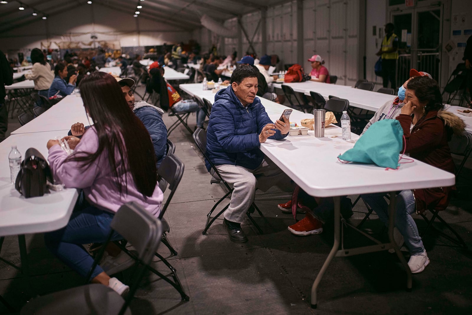 FILE - Migrant, Cesar Anibal Bonilla Estrada, 54, from Ecuador, center, checks his phone during dinner time at the migrant shelter on Randall's Island, on Tuesday, April 9, 2024, in New York. (AP Photo/Andres Kudacki, File)