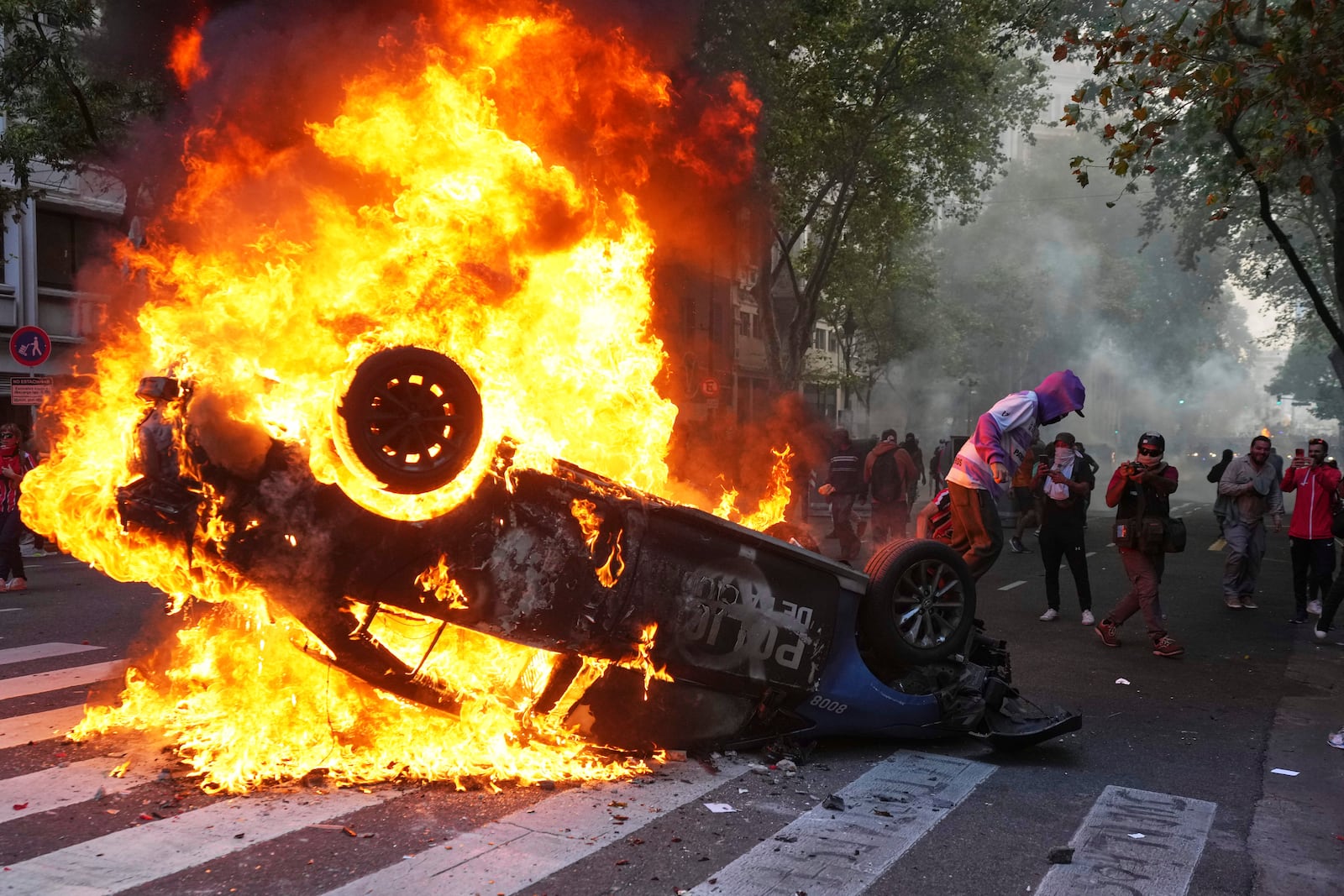 A protester burns a police car during a demonstration by soccer fans join and retirees demanding higher pensions and opposing austerity measures implemented by Javier Milei's government in Buenos Aires, Argentina, Wednesday, March 12, 2025. (AP Photo/Rodrigo Abd)