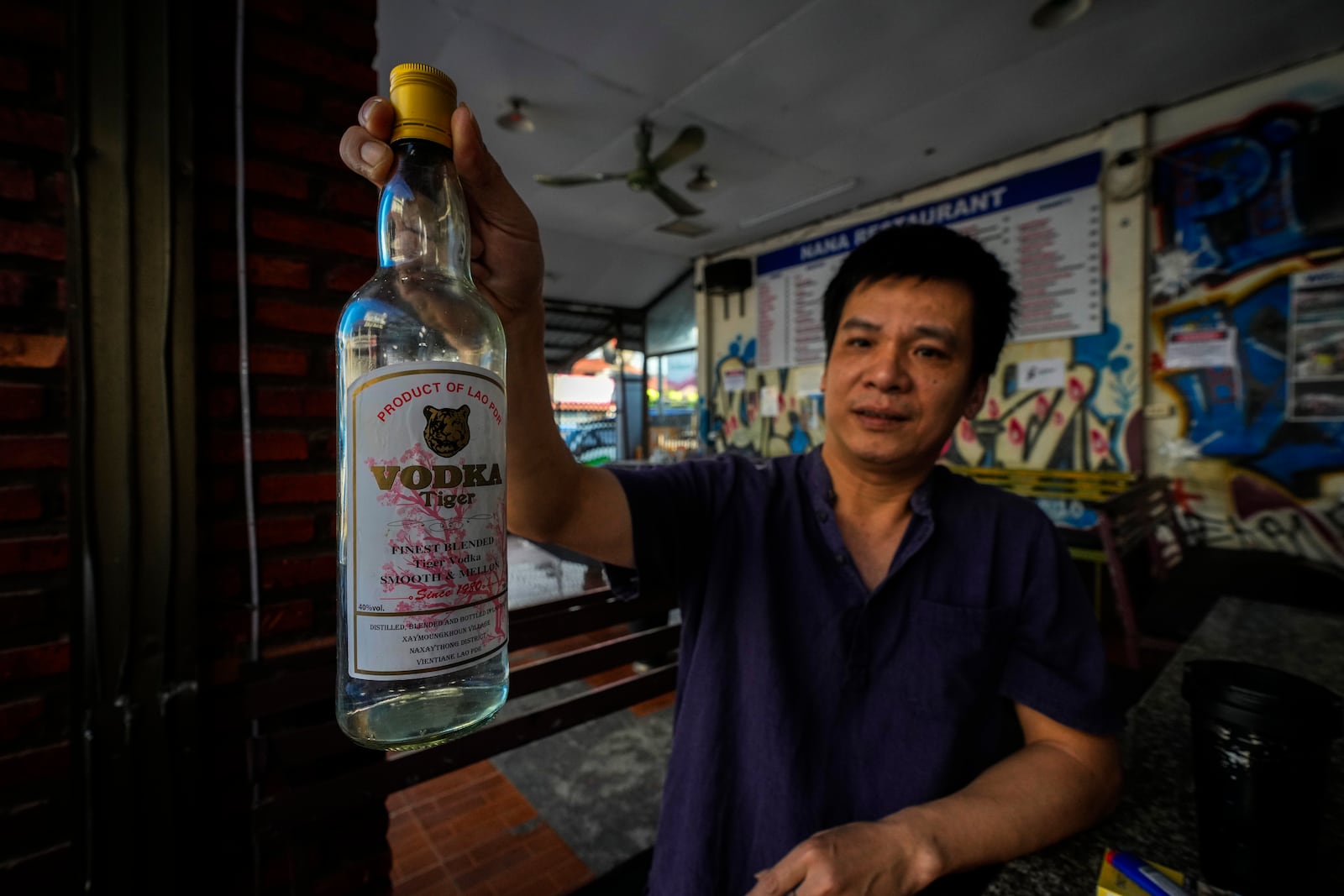 Duong Duc Toan, the manager of Nana Backpack hostel displays a bottle of vodka, in the bar of the hostel in Vang Vieng, Laos, Tuesday, Nov. 19, 2024. (AP Photo/Anupam Nath)