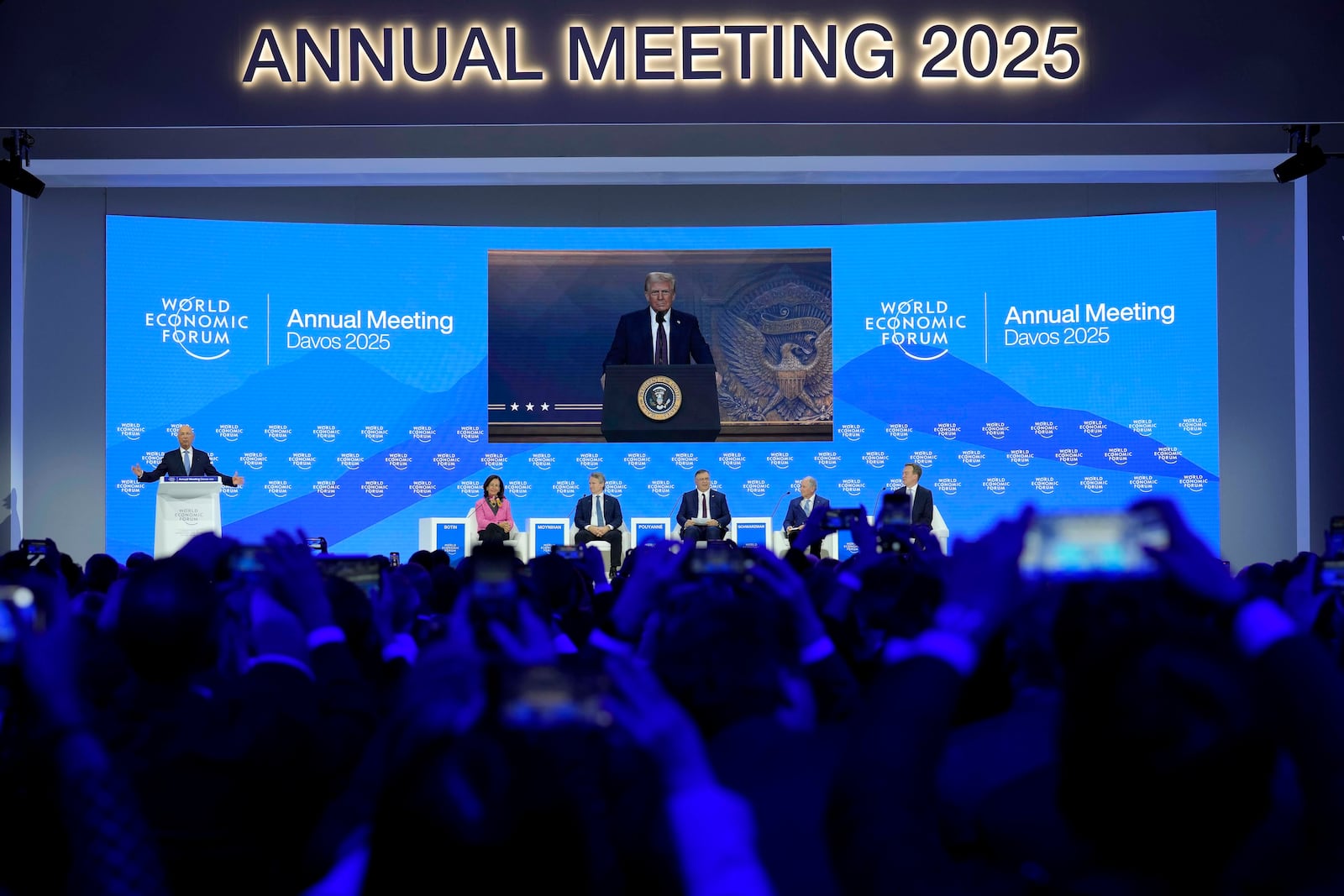 People follow a virtual speech of U.S. president Donald Trump at the Annual Meeting of World Economic Forum in Davos, Switzerland, Thursday, Jan. 23, 2025. (AP Photo/Markus Schreiber)