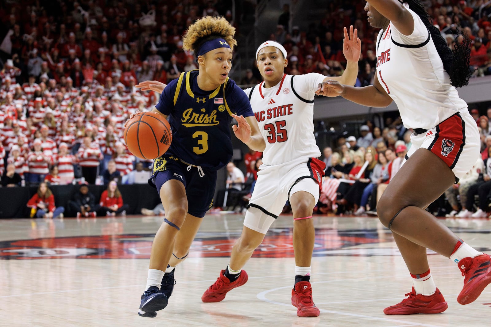 Notre Dame's Hannah Hidalgo (3) drives as NC State's Zoe Brooks (35) and Lorena Awou (1) defend during the first half of an NCAA college basketball game in Raleigh, N.C., Sunday, Feb. 23, 2025. (AP Photo/Ben McKeown)