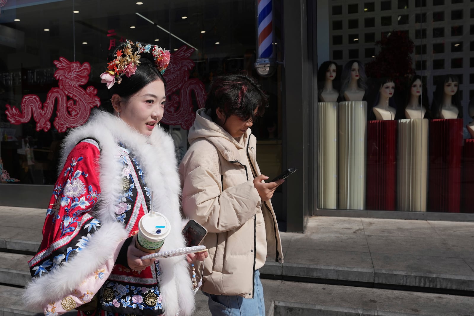 A woman wearing traditional costume passes by stores along the popular Wangfujing shopping street in Beijing, China, Thursday, March 6, 2025. (AP Photo/Ng Han Guan)