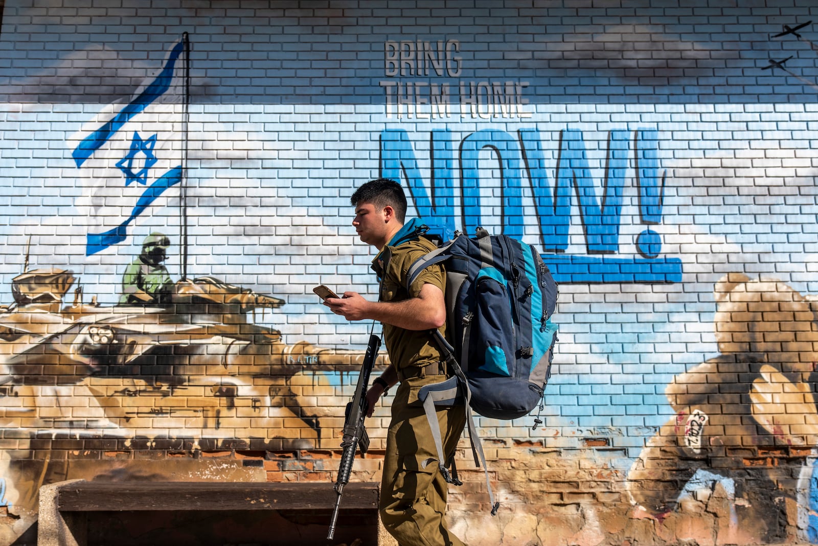 An Israeli soldier walks past a graffiti, calling for the return of the hostages kidnapped during the Oct. 7 , 2023 Hamas cross-border attacks in Israel, in Kfar Saba, Israel, Sunday, Jan. 19, 2025. (AP Photo/Ariel Schalit)