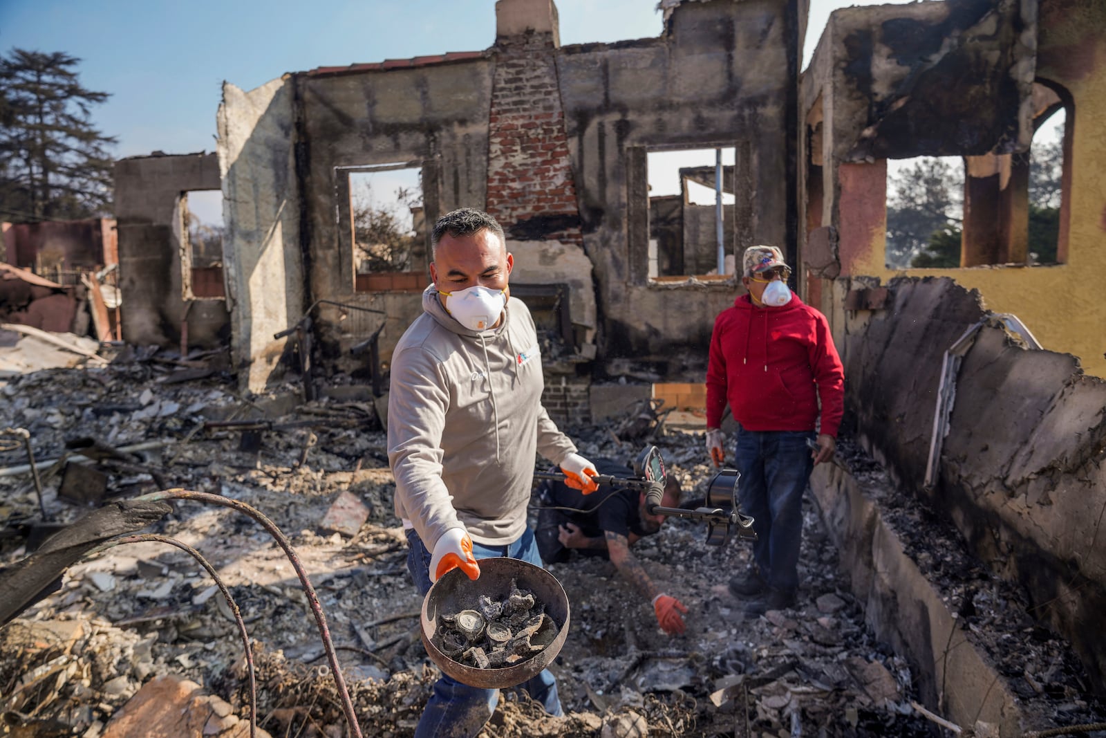 Homeowner David Marquez, left, holds a metal detector as he shows recovered metal items found with his father, Juan Pablo Alvarado, right, inside the walls of their multi-generational home in the aftermath of the Eaton Fire, Sunday, Jan. 19, 2025, in Altadena, Calif. (AP Photo/Damian Dovarganes)