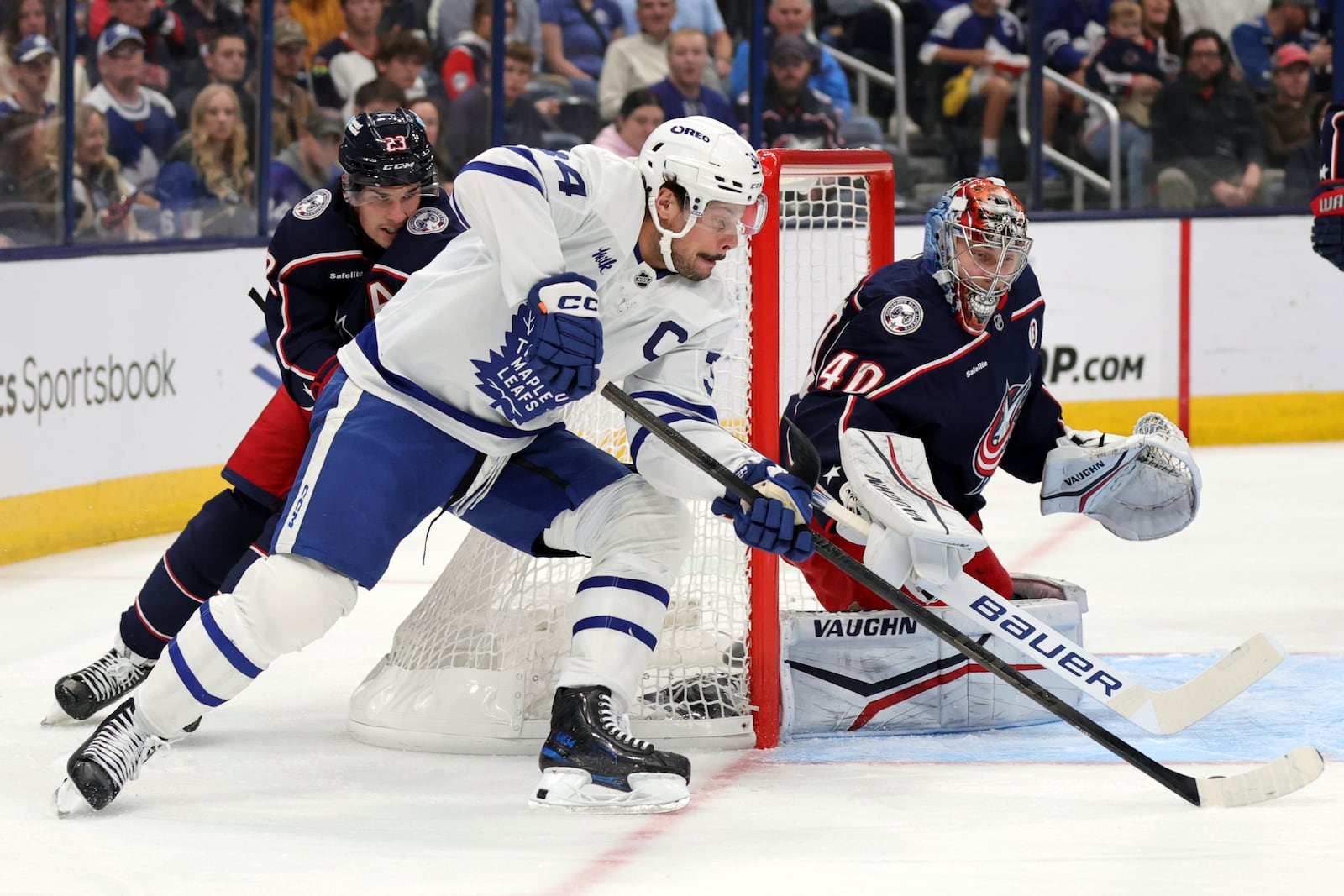 Toronto Maple Leafs forward Auston Matthews, center, controls the puck between Columbus Blue Jackets defenseman Sean Monahan, left, and goalie Daniil Tarasov during the first period of an NHL hockey game in Columbus, Ohio, Tuesday, Oct. 22, 2024. (AP Photo/Paul Vernon)