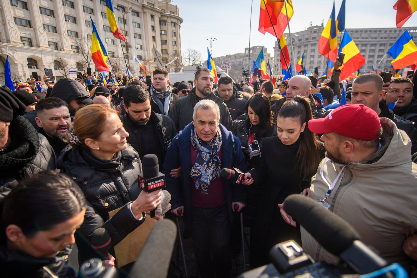 FILE - Calin Georgescu, the winner of Romania's first round of presidential election, annulled by the Constitutional Court, uses crutches walking between supporters gathered for a protest outside the Romanian parliament in Bucharest, Romania, Saturday, Feb. 22, 2025. (AP Photo/Alexandru Dobre, File)