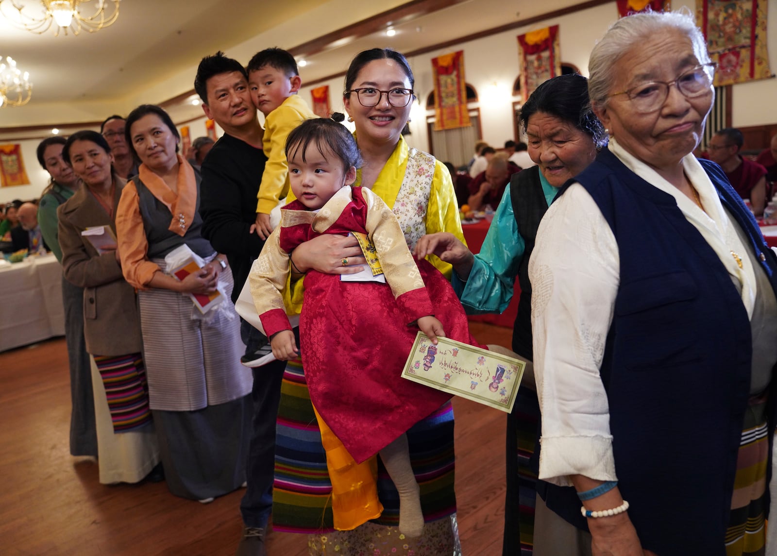 Tenzin Lhasa holds her daughter, Dawoe Tenzin Arya, while in procession to present U.S.-born Buddhist lama, Jalue Dorje, with “khata,” the Tibetan ceremonial scarves that symbolize auspiciousness, at his 18th birthday and enthronement ceremony, in Isanti, Minn., on Saturday, Nov. 9, 2024. (AP Photo/Jessie Wardarski)