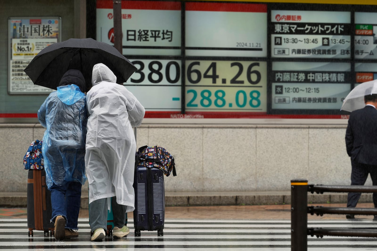 Travelers walk by monitors showing Japan's Nikkei 225 index at a securities firm in Tokyo, Thursday, Nov. 21, 2024. (AP Photo/Hiro Komae)