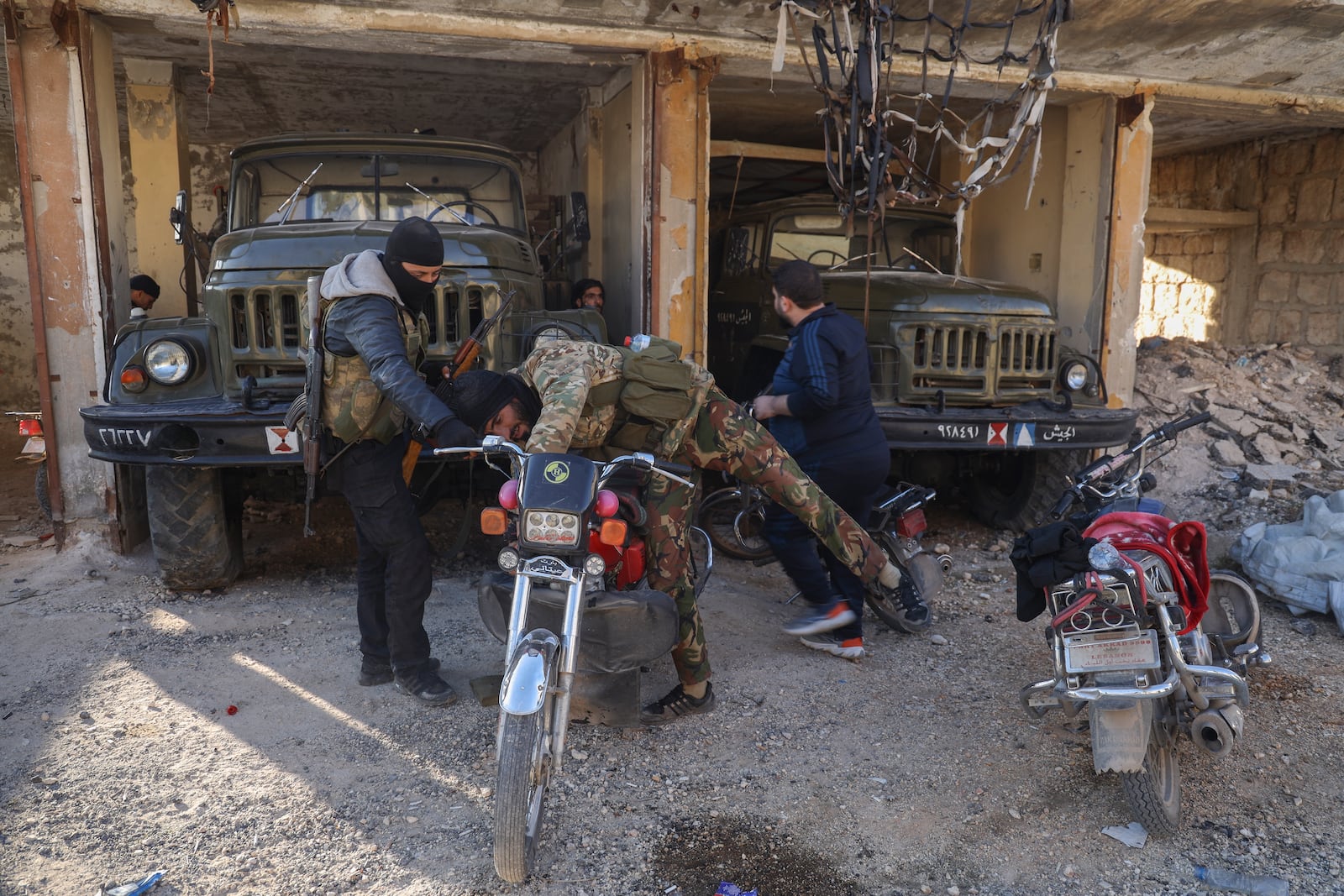 A Syrian opposition fighter checks a motorcycle next to abandoned army vehicles in the town of Maarat al-Numan, southwest of Aleppo, Syria, Saturday Nov. 30, 2024. Thousands of Syrian insurgents have fanned out inside Syria's largest city Aleppo and large areas around previously controlled by the government with little resistance from troops.(AP Photo/Omar Albam)