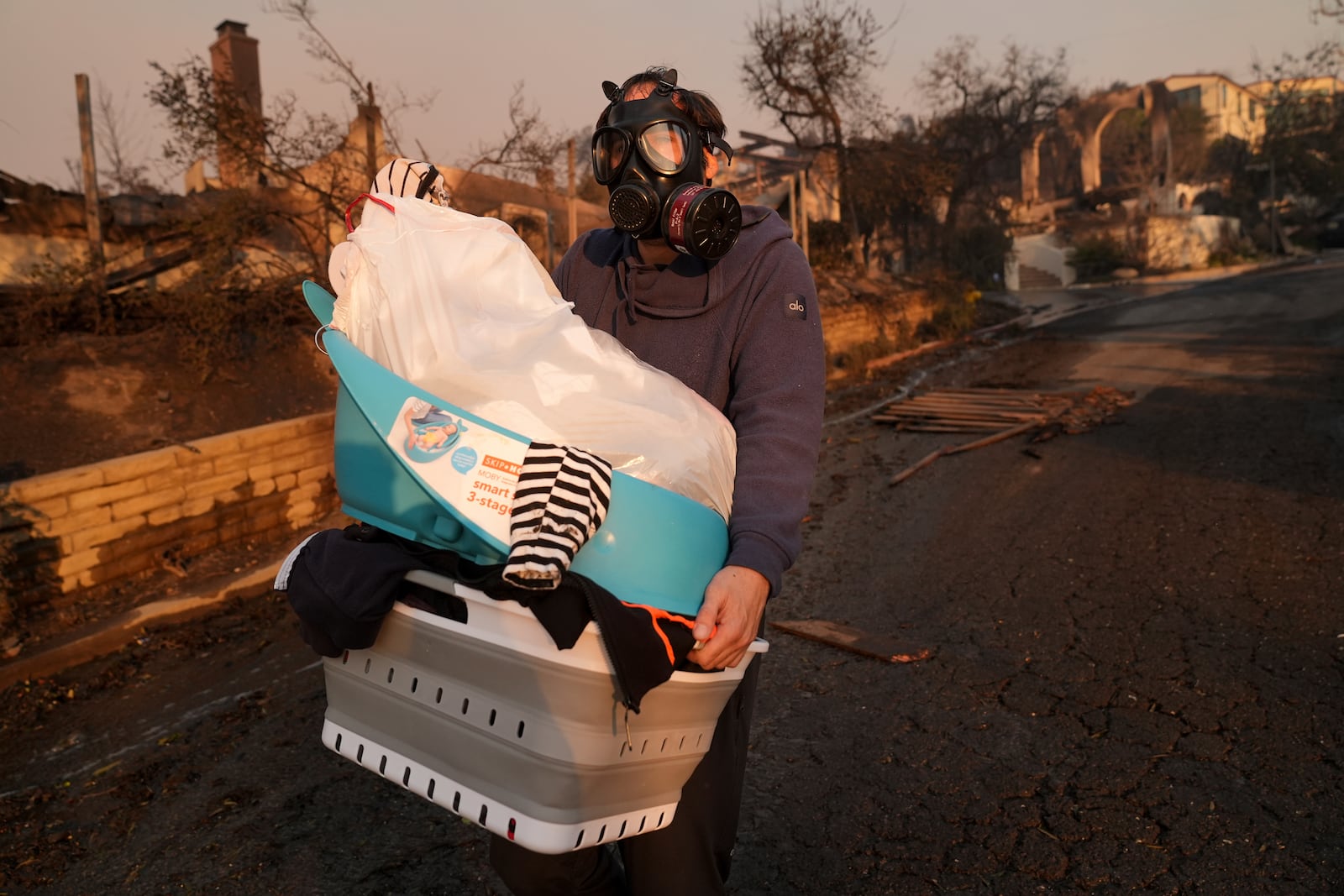 Josh Lederer wears a mask to protect him from fumes as he retrieves his children's clothes from his fire-raved property in the aftermath of the Palisades Fire in the Pacific Palisades neighborhood of Los Angeles, Thursday, Jan. 9, 2025. (AP Photo/Jae C. Hong)