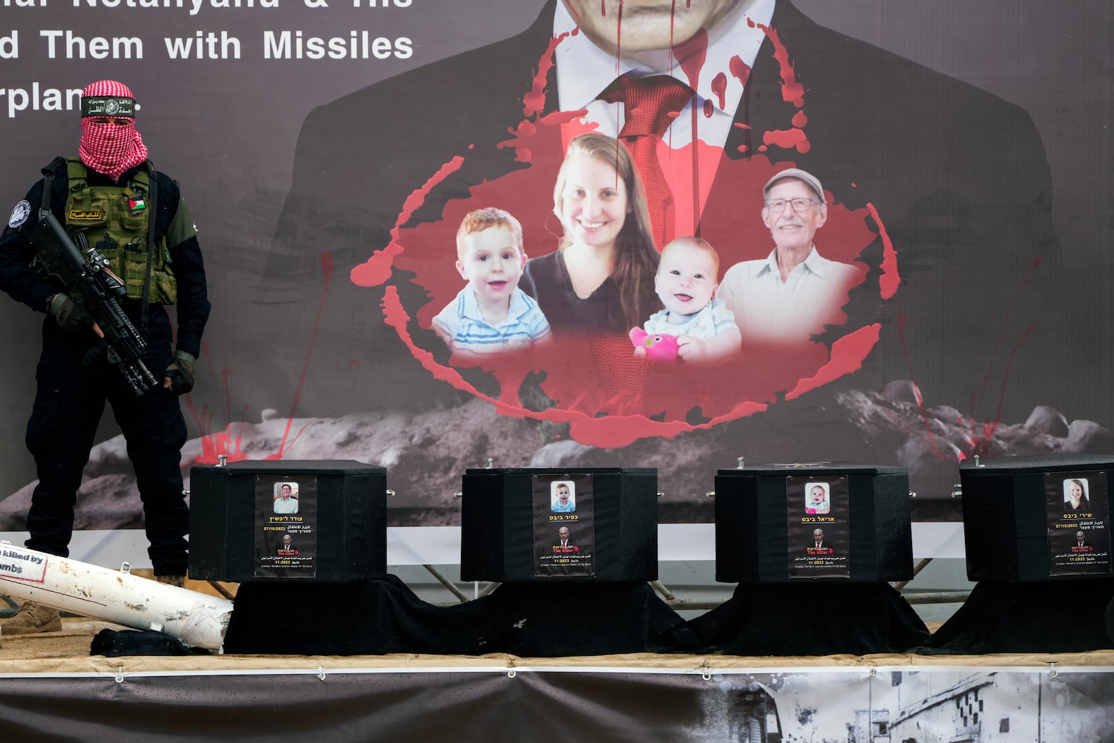 A militant stands next to the coffins containing the bodies of four Israeli hostages, including a mother and her two children before their are handed over to the Red Cross in Khan Younis, southern Gaza Strip, Thursday, Feb. 20, 2025. (AP Photo/Abdel Kareem Hana)