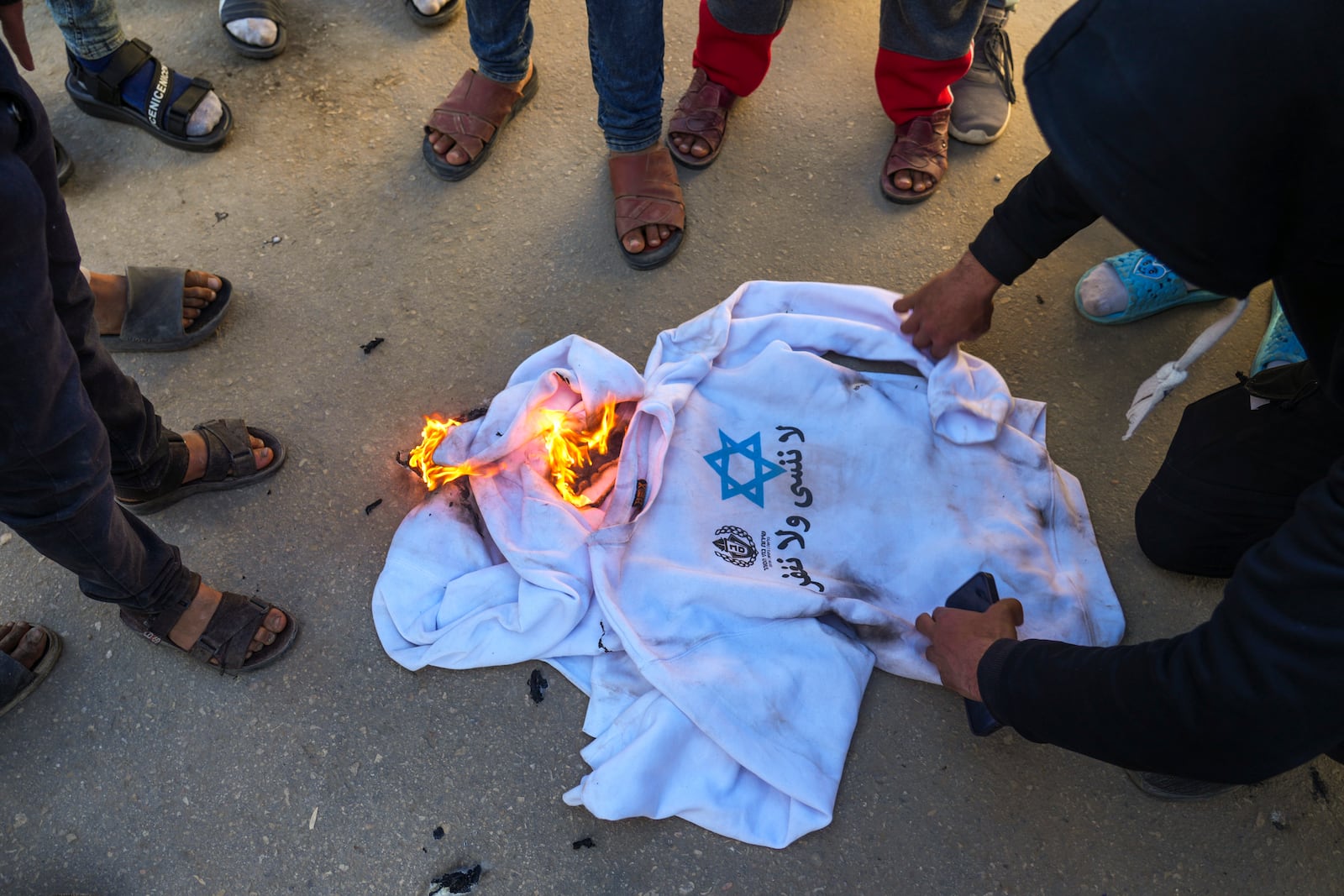 A crowd burns the shirts worn by freed Palestinian prisoners in Khan Younis, Gaza Strip, Saturday, Feb. 15, 2025, as they arrive in Gaza after being released from an Israeli prison following a ceasefire agreement between Hamas and Israel. (AP Photo/Abdel Kareem Hana)