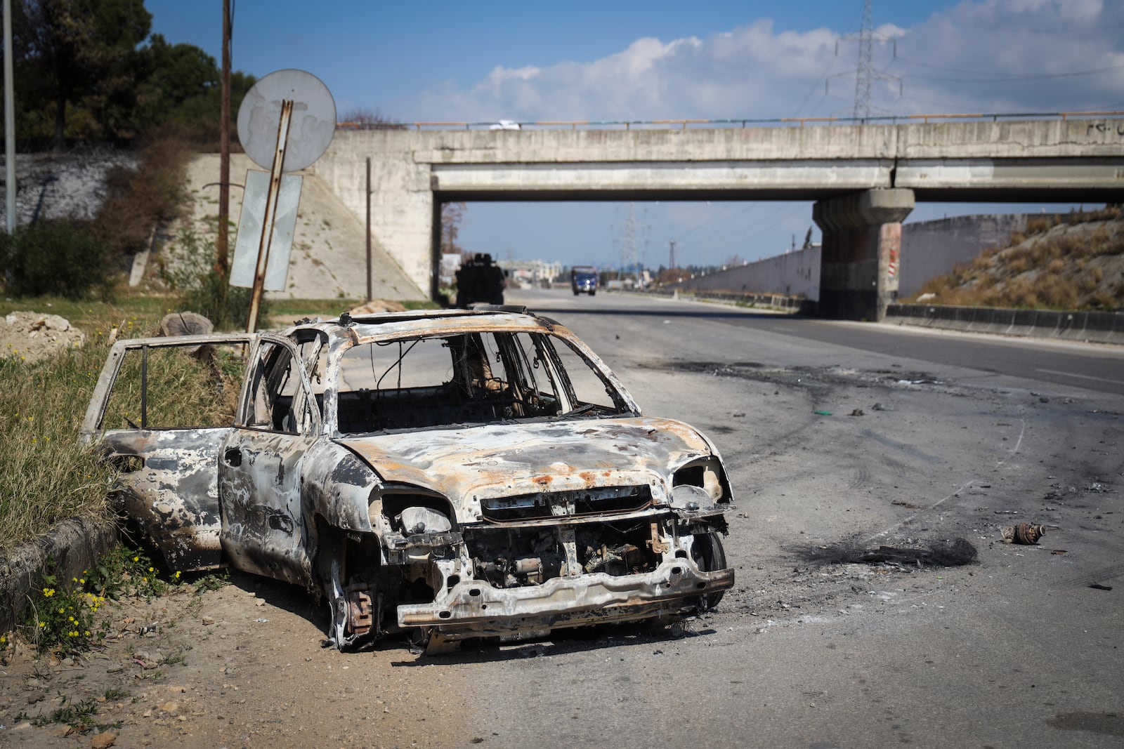 A burnt car remains in the middle of a empty road following the recent wave of violence between Syrian security forces and gunmen loyal to former President Bashar Assad, as well as subsequent sectarian attacks, in the outskirts of the village of Qardaha, the birthplace of Assad, Monday, March 10, 2025. (AP Photo/Omar Albam)