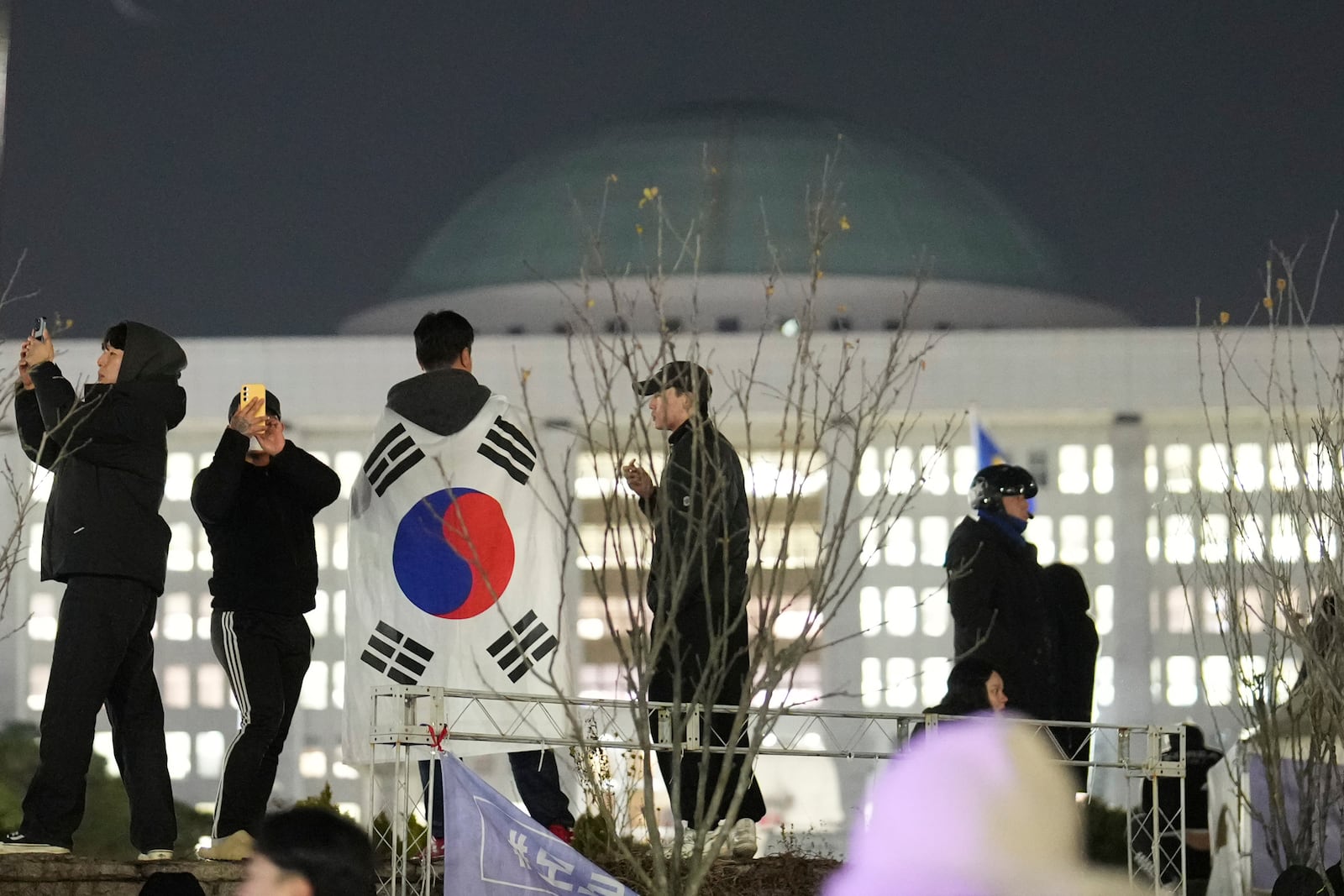 A man wearing a national flag stands on the wall of the National Assembly in Seoul, South Korea, Wednesday, Dec. 4, 2024. (AP Photo/Lee Jin-man)