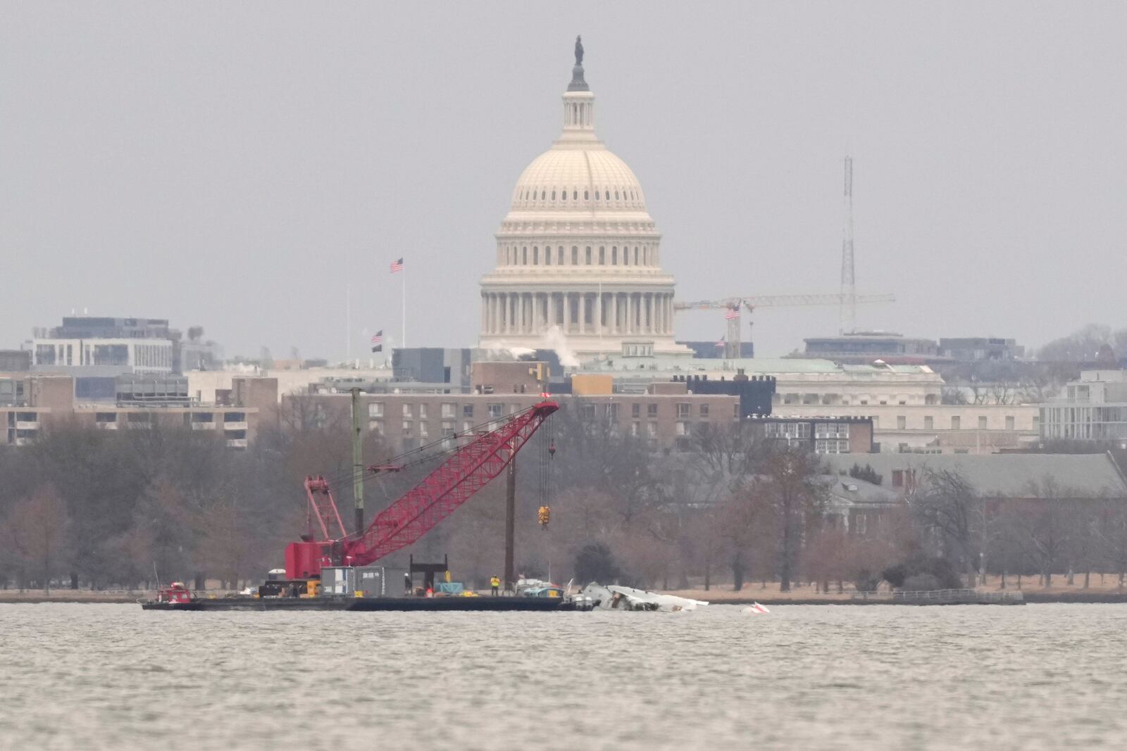 With the U.S. Capitol in the background, a crane sits in the Potomac river Sunday, Feb. 2, 2025, near the wreckage of an American Airlines jet that collided mid-air with an Army Black Hawk helicopter in Arlington, Va., as seen from Alexandria, Va. (AP Photo/Carolyn Kaster)