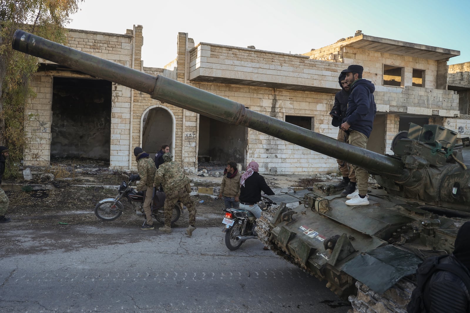 Syrian opposition fighters get on a motorcycle as opposition supporters stand on top of a captured army armoured vehicle in the town of Maarat al-Numan, southwest of Aleppo, Syria, Saturday Nov. 30, 2024. Thousands of Syrian insurgents have fanned out inside Syria's largest city Aleppo and large areas around previously controlled by the government with little resistance from troops.(AP Photo/Omar Albam)