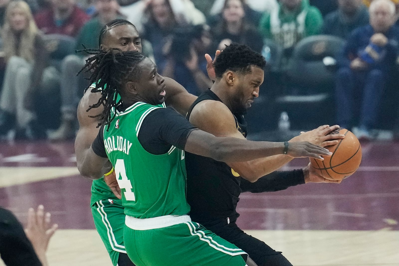 Cleveland Cavaliers guard Donovan Mitchell, right, is pressured by Boston Celtics guard Jaylen Brown, rear, and guard Jrue Holiday (4) in the first half of an NBA basketball game, Tuesday, Feb. 4, 2025, in Cleveland. (AP Photo/Sue Ogrocki)