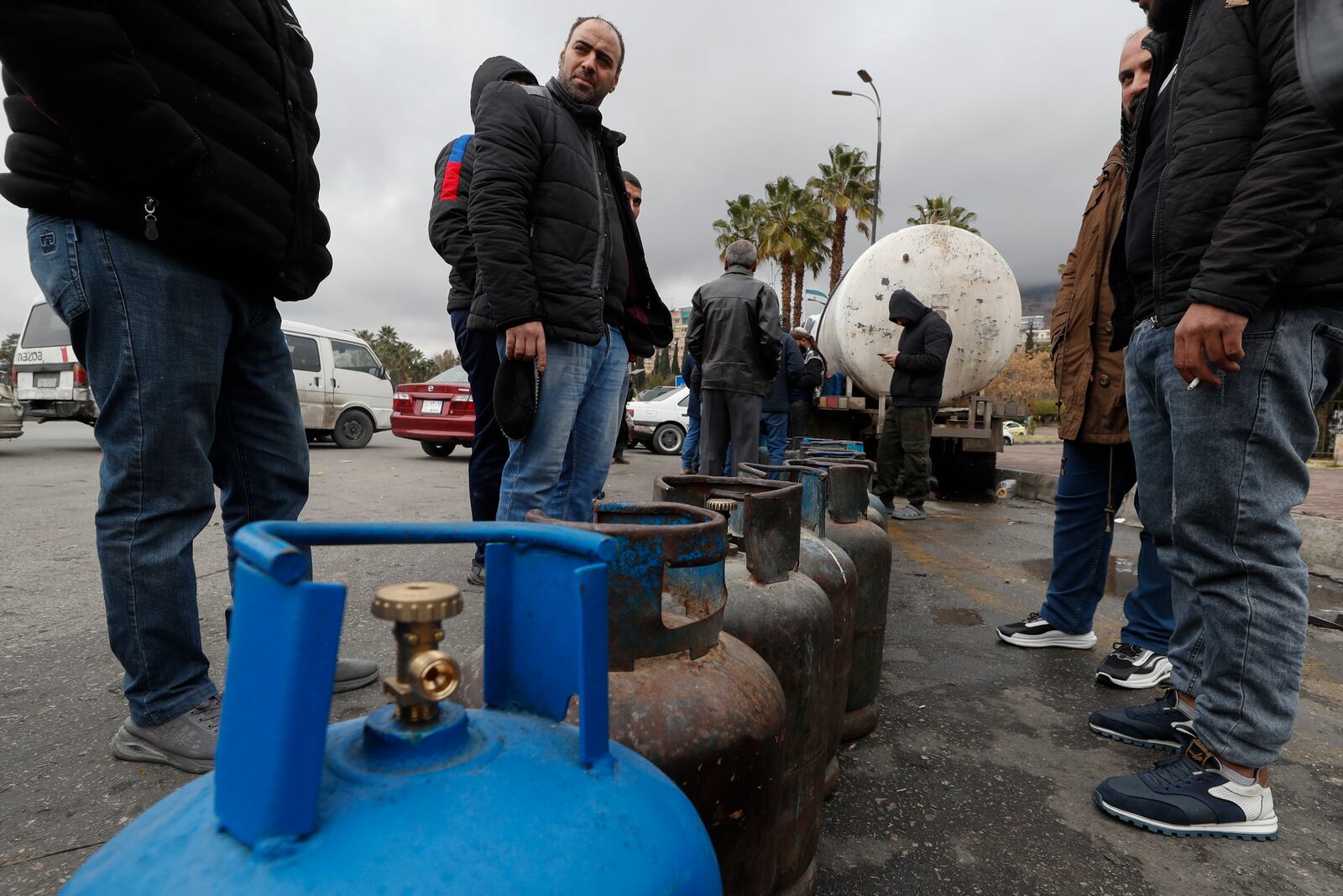 People stand next to propane cylinders as they wait in line to buy gas on a street at the Umayyad Square in Damascus, Syria, Saturday, Dec. 28, 2024. (AP Photo/Omar Sanadiki)