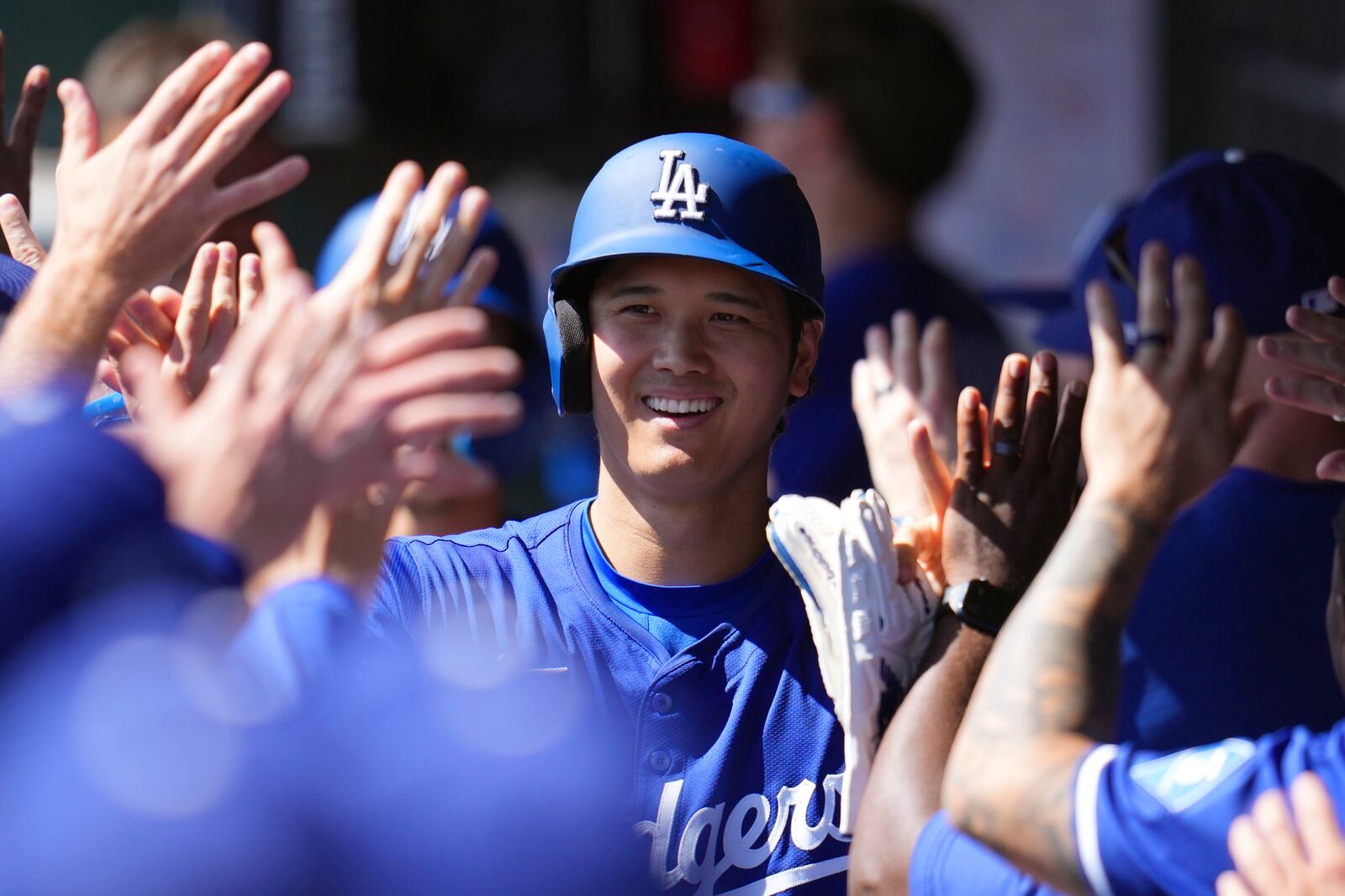 Los Angeles Dodgers' Shohei Ohtani, of Japan, smiles as he celebrates with teammates after scoring a run on a two-run home run by Dodgers' Tommy Edman during the first inning of a spring training baseball game against the Cleveland Guardians, Tuesday, March 11, 2025, in Phoenix. (AP Photo/Ross D. Franklin)